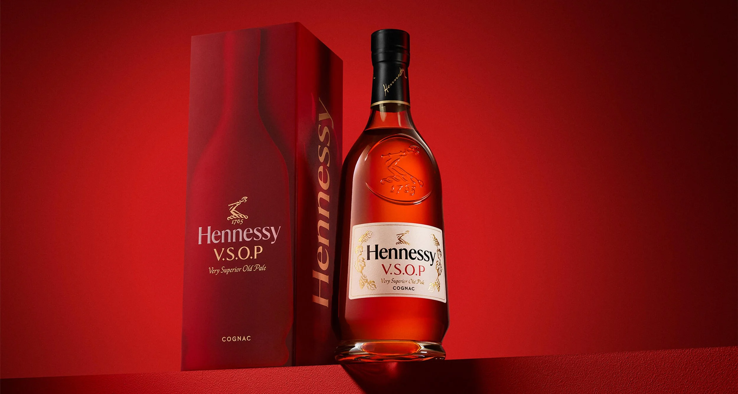 A bottle of Hennessy V.S.O.P cognac with its red packaging box, set against a red background.