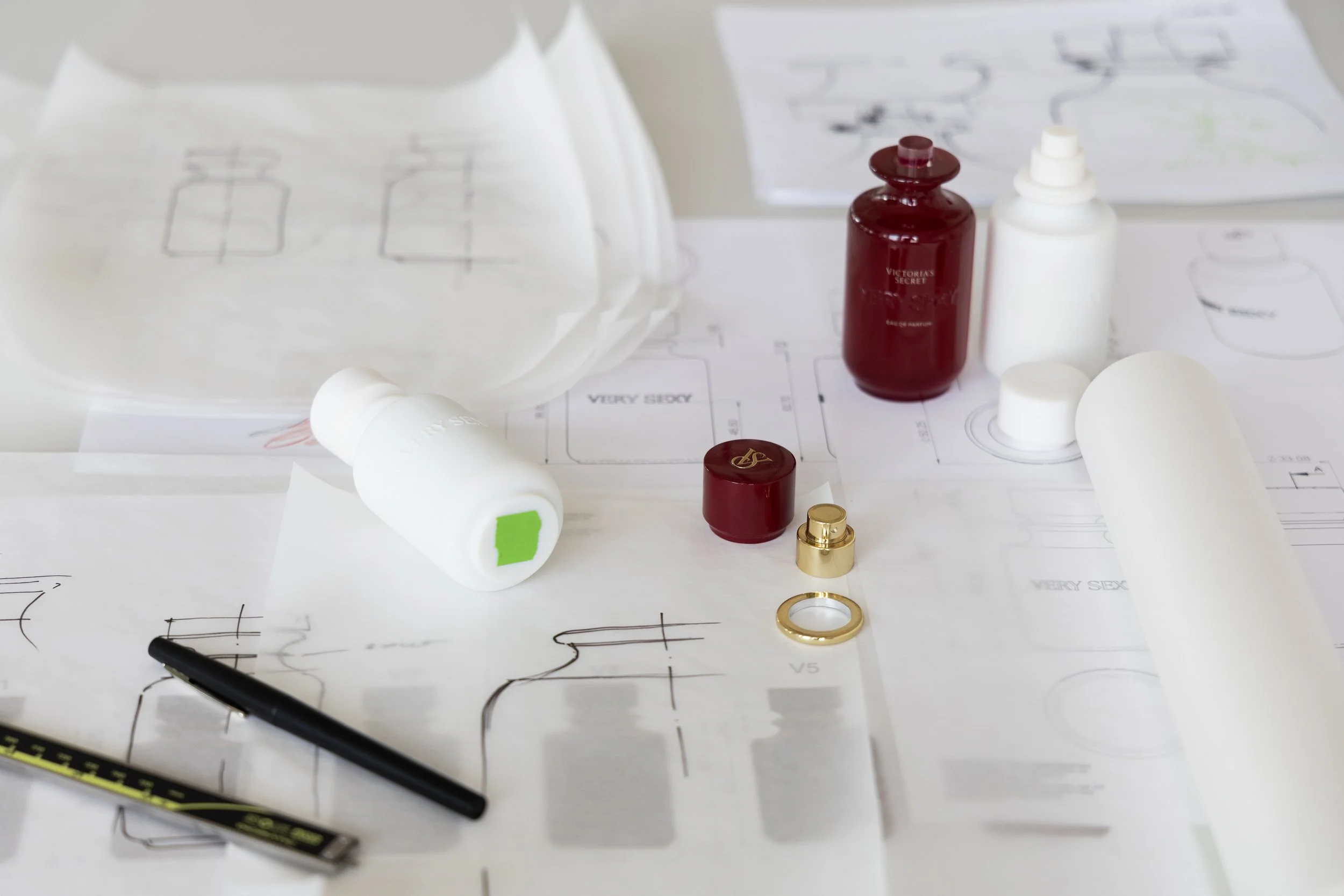 Design plans and sketches of a perfume bottle with bottle models, 3d prints, and a pen on a desk.