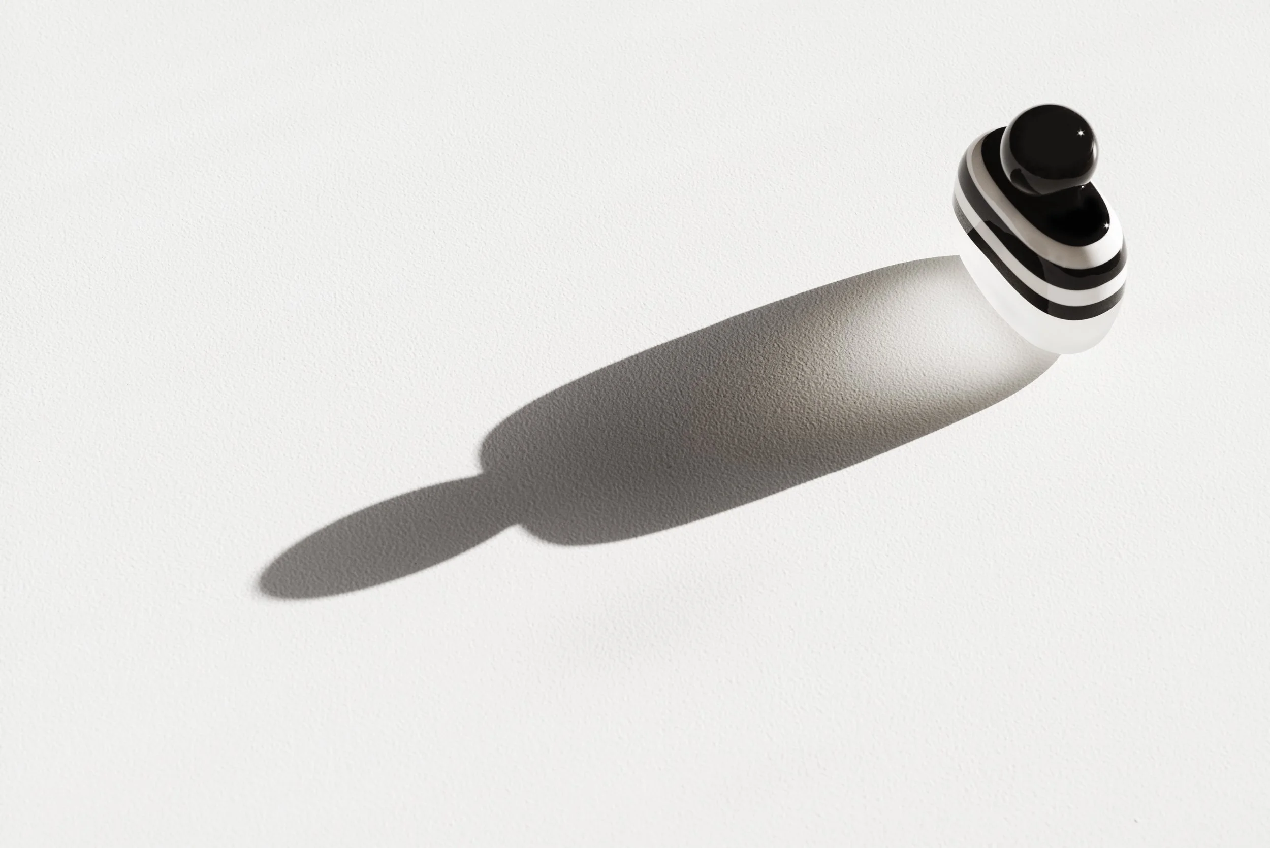 A black and white striped fragrance bottle casting a shadow on a white textured surface.