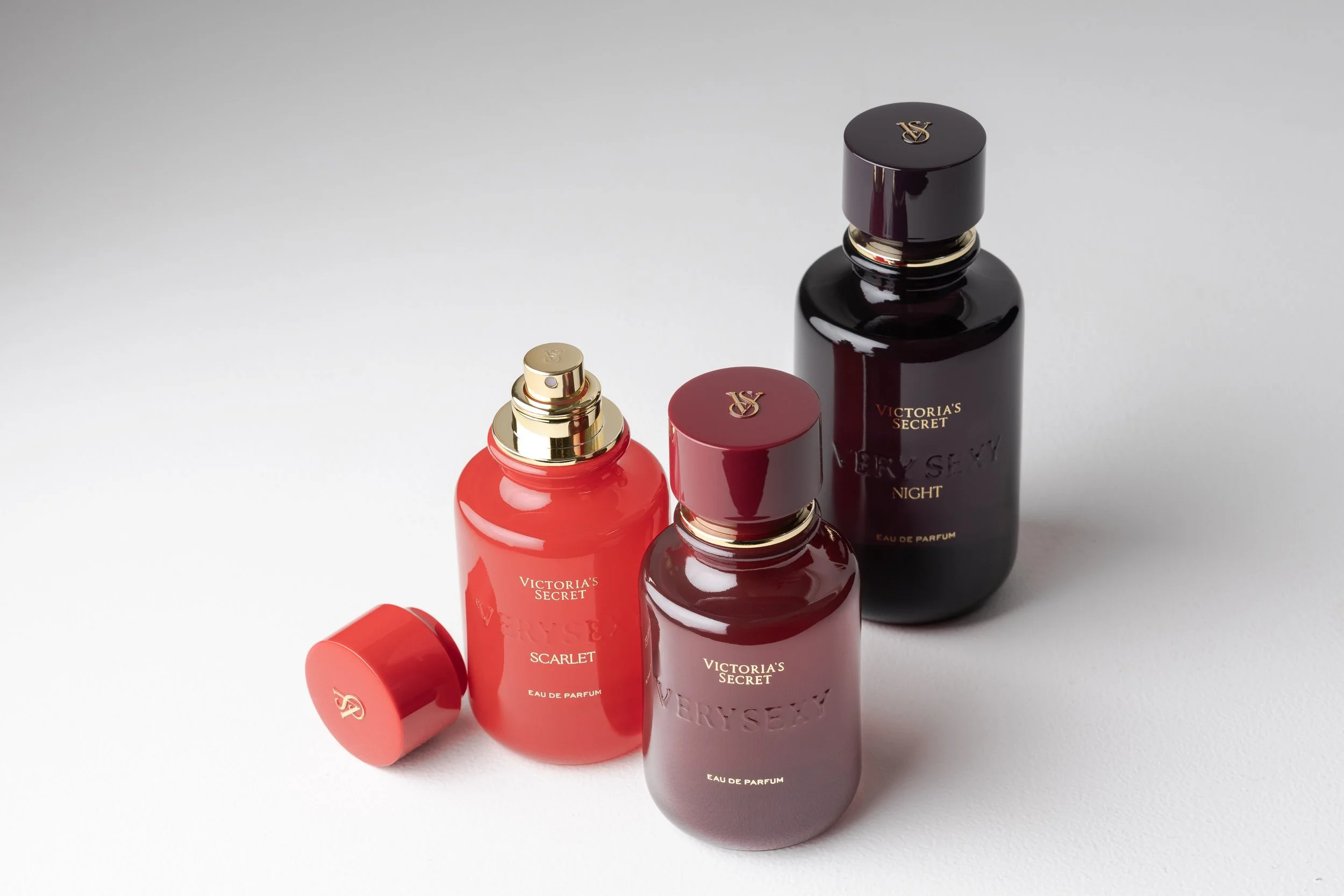 Three bottles of Victoria's Secret perfume, with varying colors and sizes, placed on a white surface.