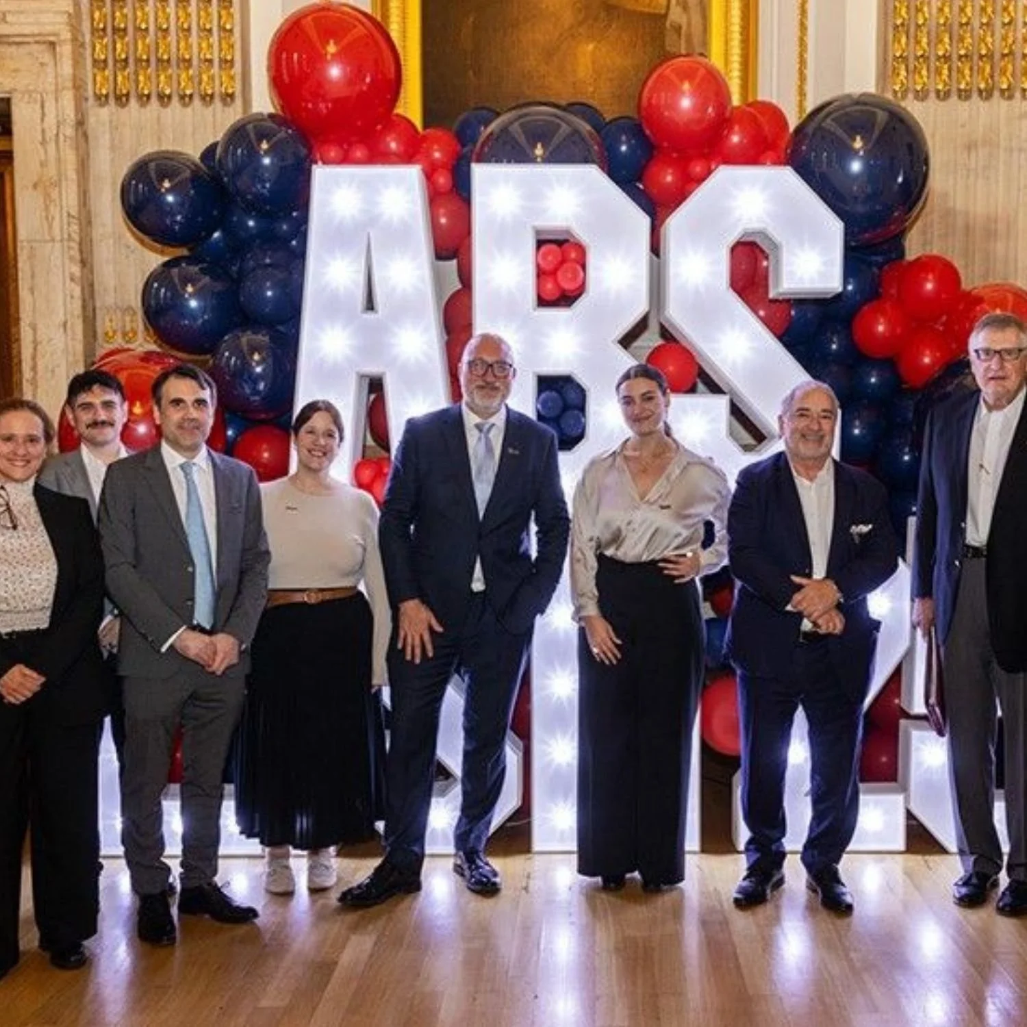 Group of people standing in front of large illuminated letters and balloon decorations at a celebration or event.