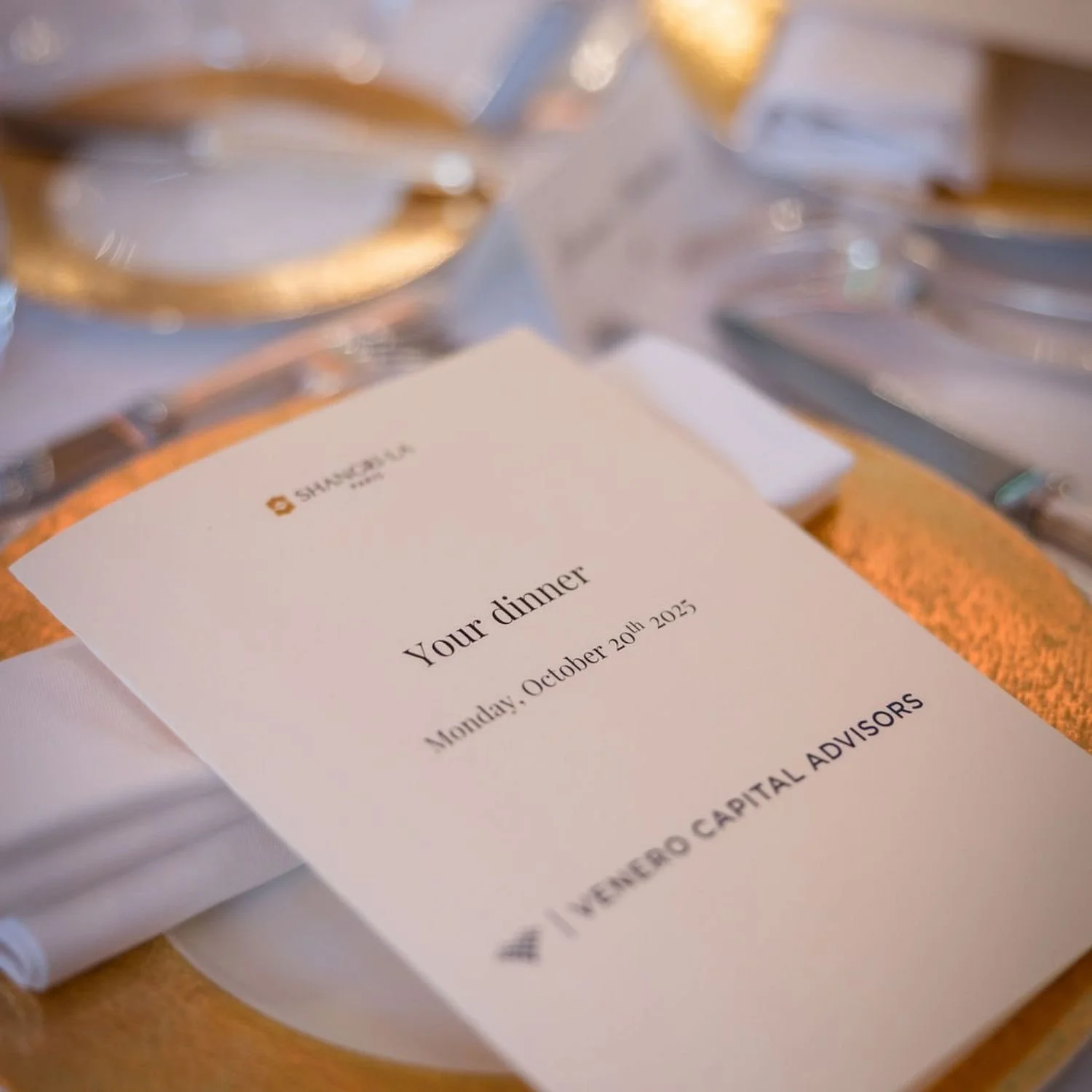 A dinner invitation card placed on a table, reading "Your dinner" for Monday, October 20th, 2025, with the logo and name of NENERO CAPITAL ADVISORS.
