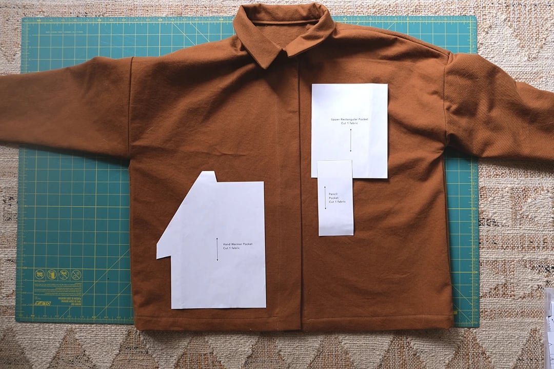Brown shirt laid flat on a cutting mat with sewing pattern pieces pinned on it.