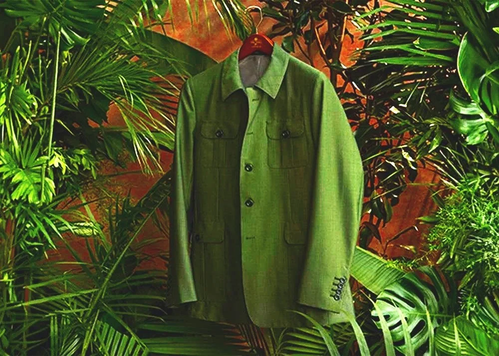 Green jacket hanging on a red hanger against tropical foliage background.