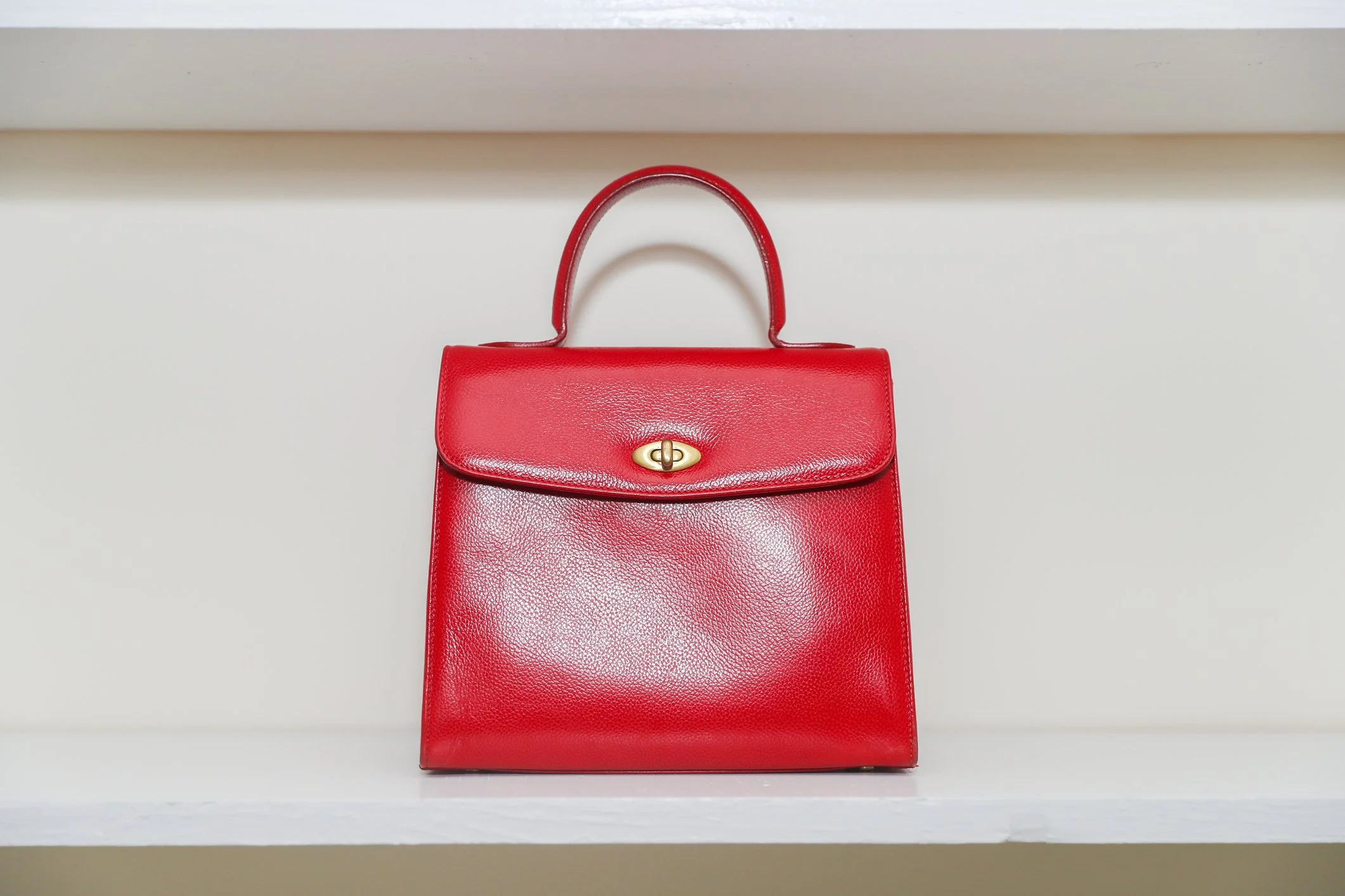 A red leather handbag with a gold clasp resting on a white shelf.
