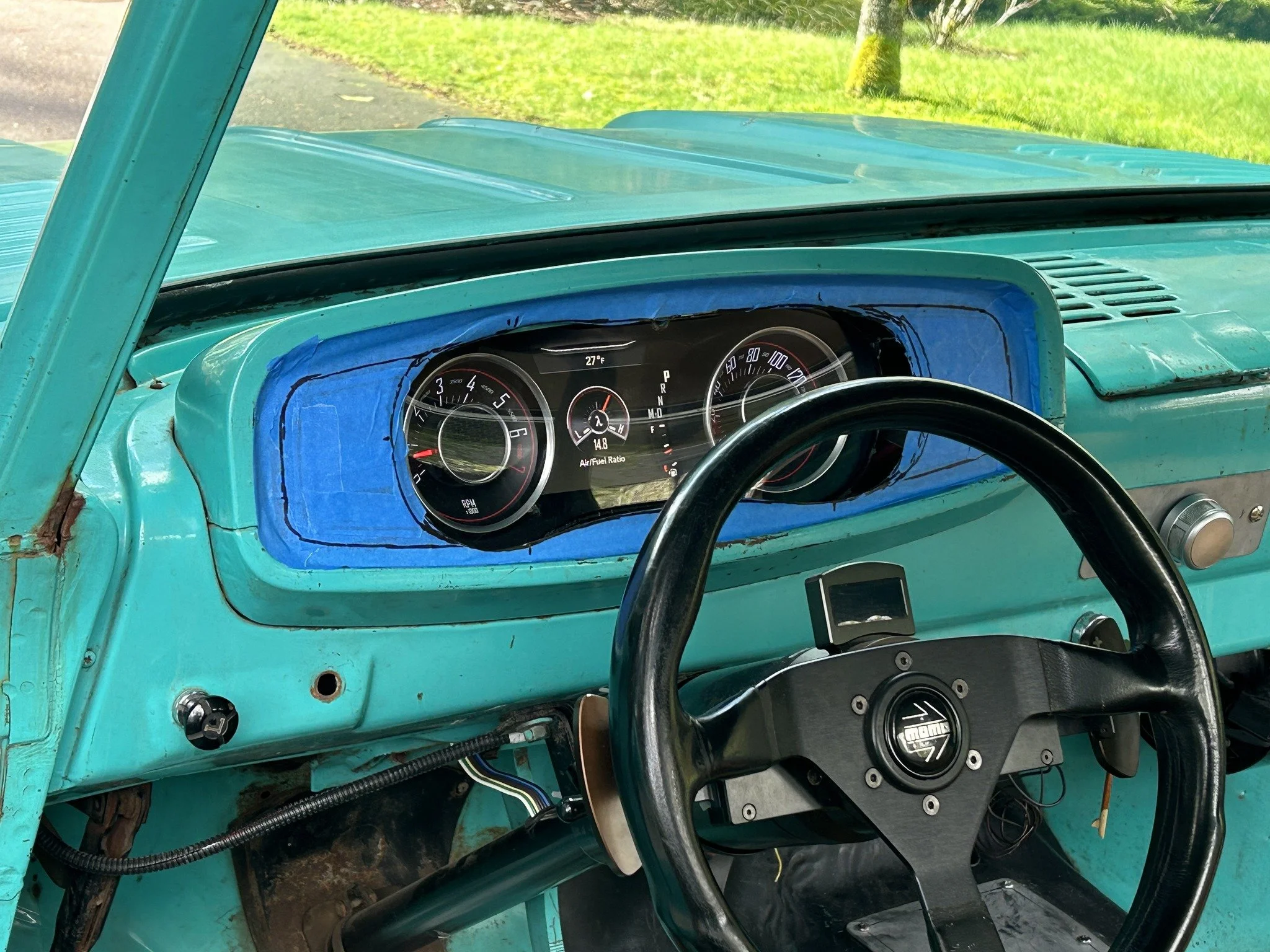 Close-up of a vintage turquoise car dashboard showing speedometer, tachometer, and digital displays, with a black steering wheel and some wiring beneath