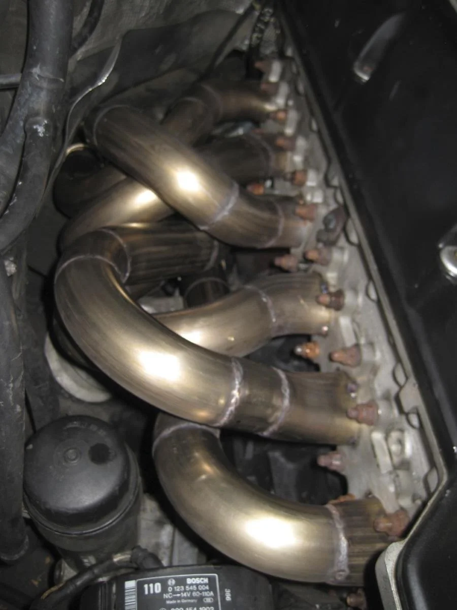 Inside an engine bay showing a set of custom metallic exhaust headers attached to the engine.
