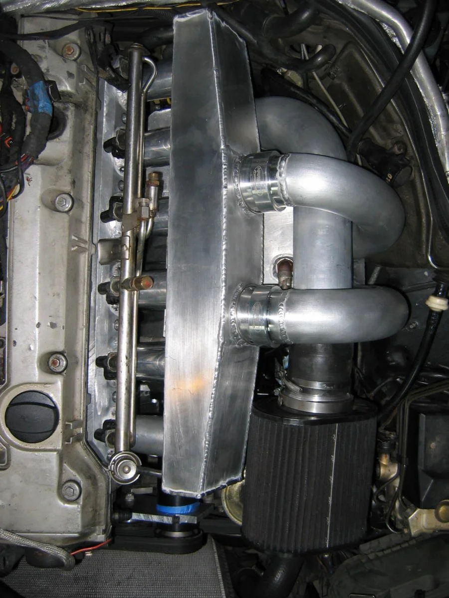 Close-up of an engine with a custom metal intake manifold and turbo piping system.