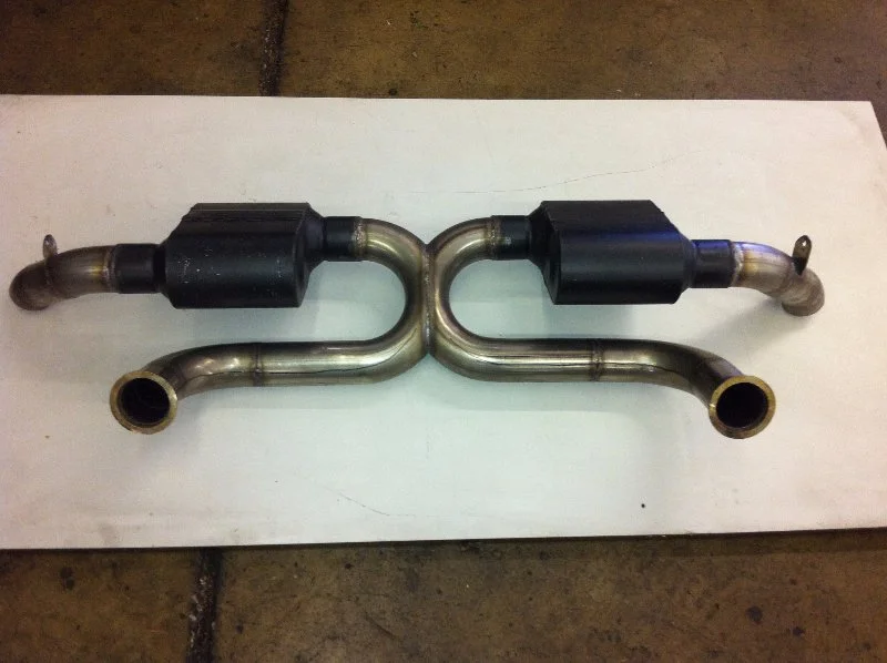 An automotive exhaust system component with pipes and mufflers, placed on a white surface.