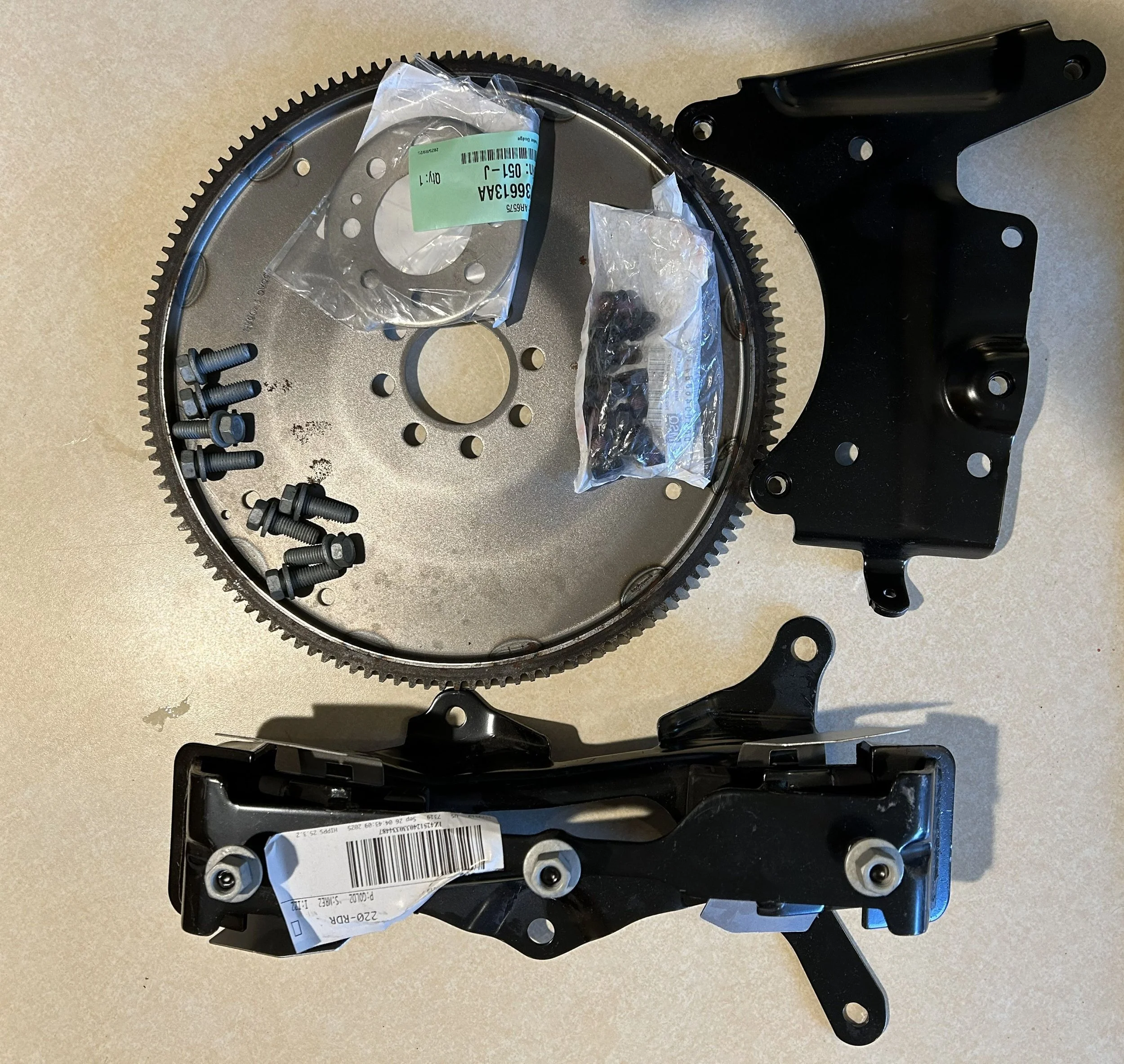 Disassembled motorcycle or bicycle engine components including a large gear, black metal brackets, screws, and small parts on a light-colored surface.
