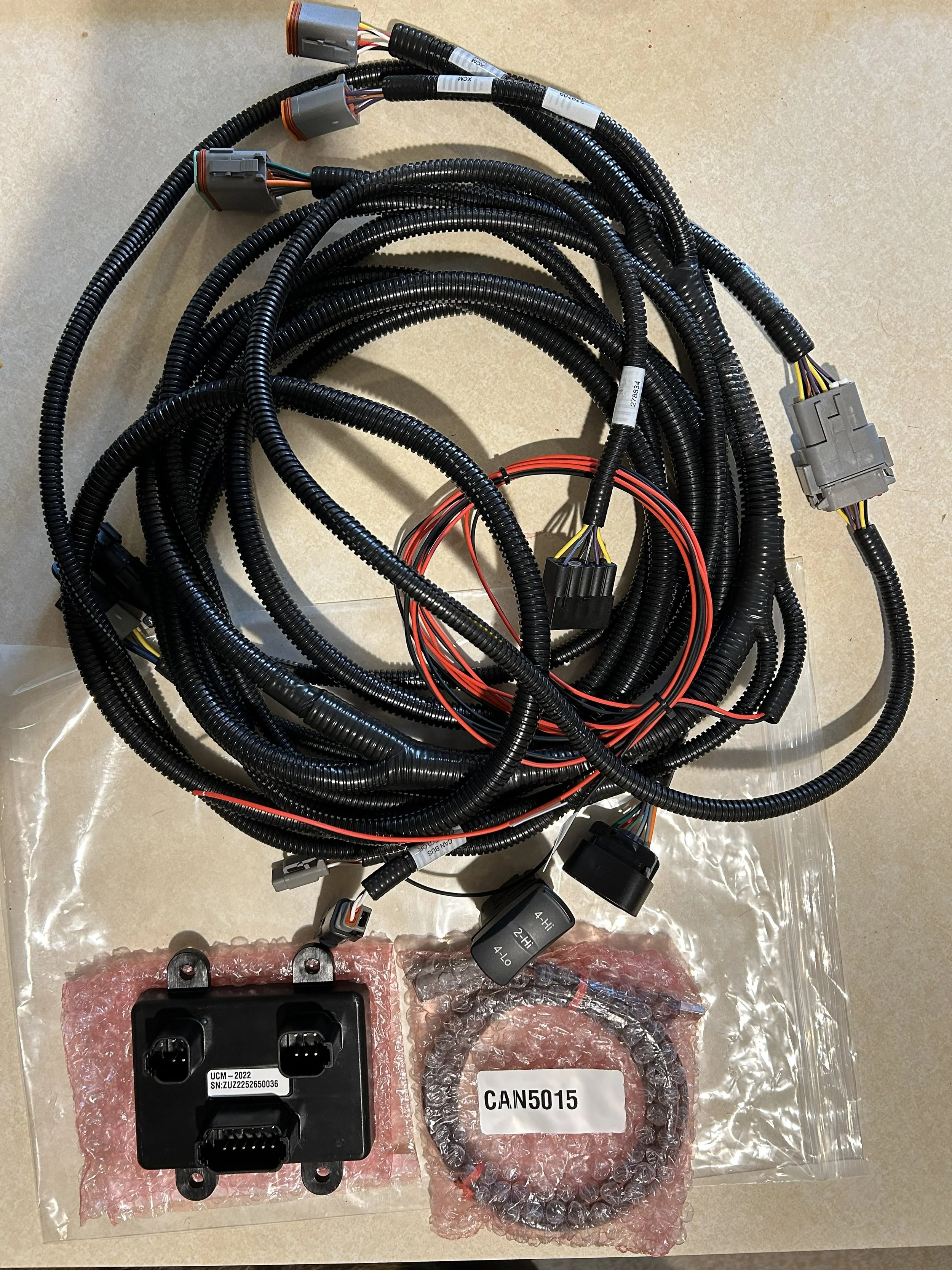 A bundle of black electrical cables and connectors, including a black electronic control module, a circular wiring harness, and other electrical components, laid out on a beige surface.