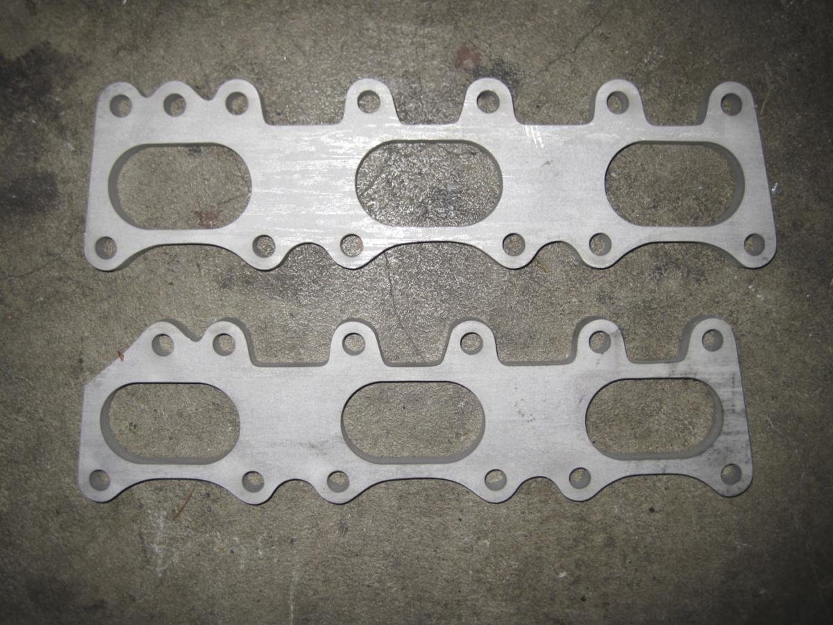 Two metallic cylinder head gaskets placed on a concrete surface.