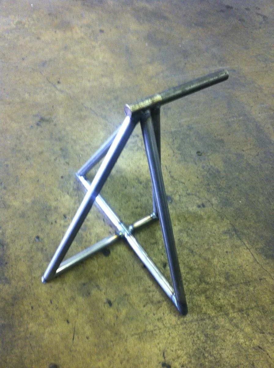 Metal stand or frame with three legs on a wooden surface.