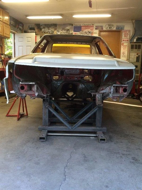 A vintage car body on a repair stand inside a garage. The car is stripped down with no front end, and is in the process of restoration or repair.