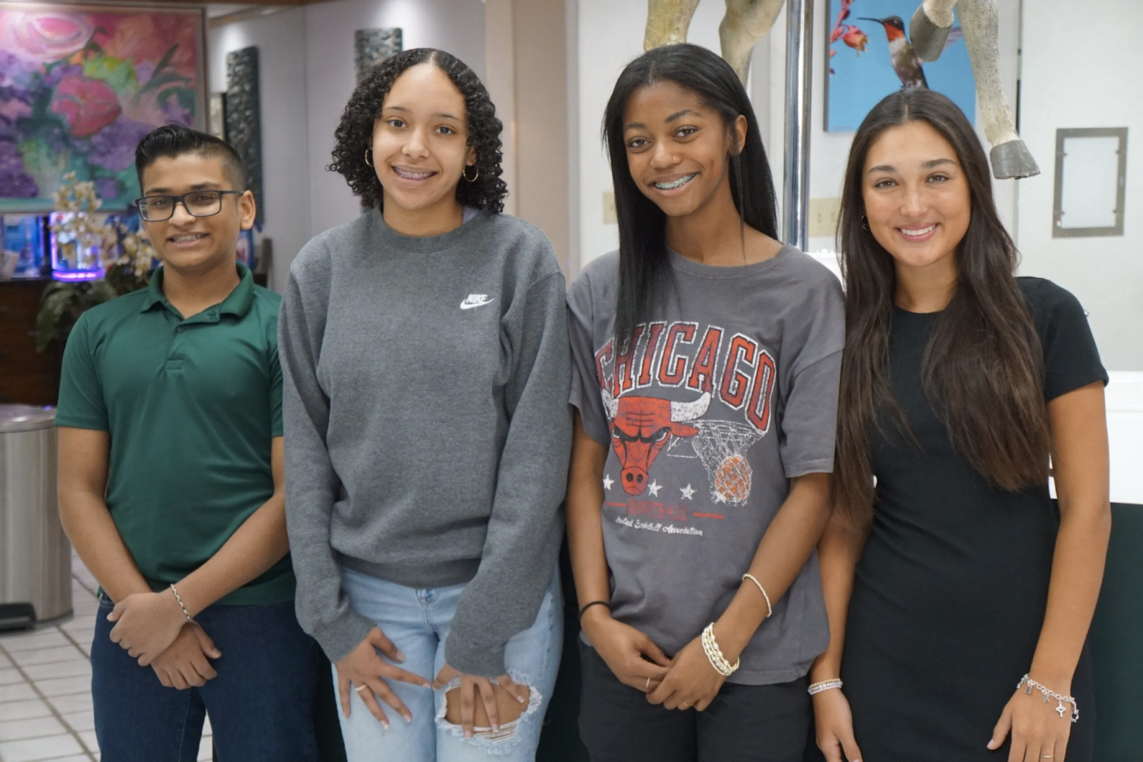 Four teenagers standing indoors, smiling at the camera.