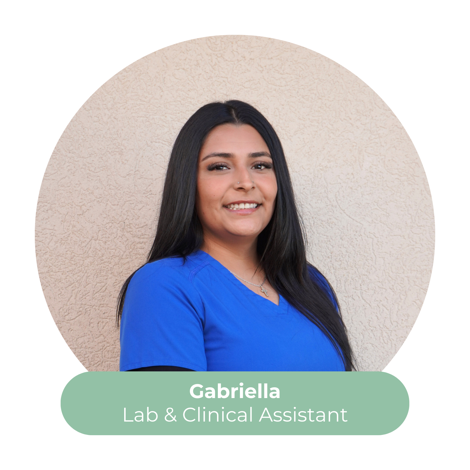 Photo of Gabriella, a Lab and Clinical Assistant, smiling and wearing blue scrubs, with a beige textured wall in the background.
