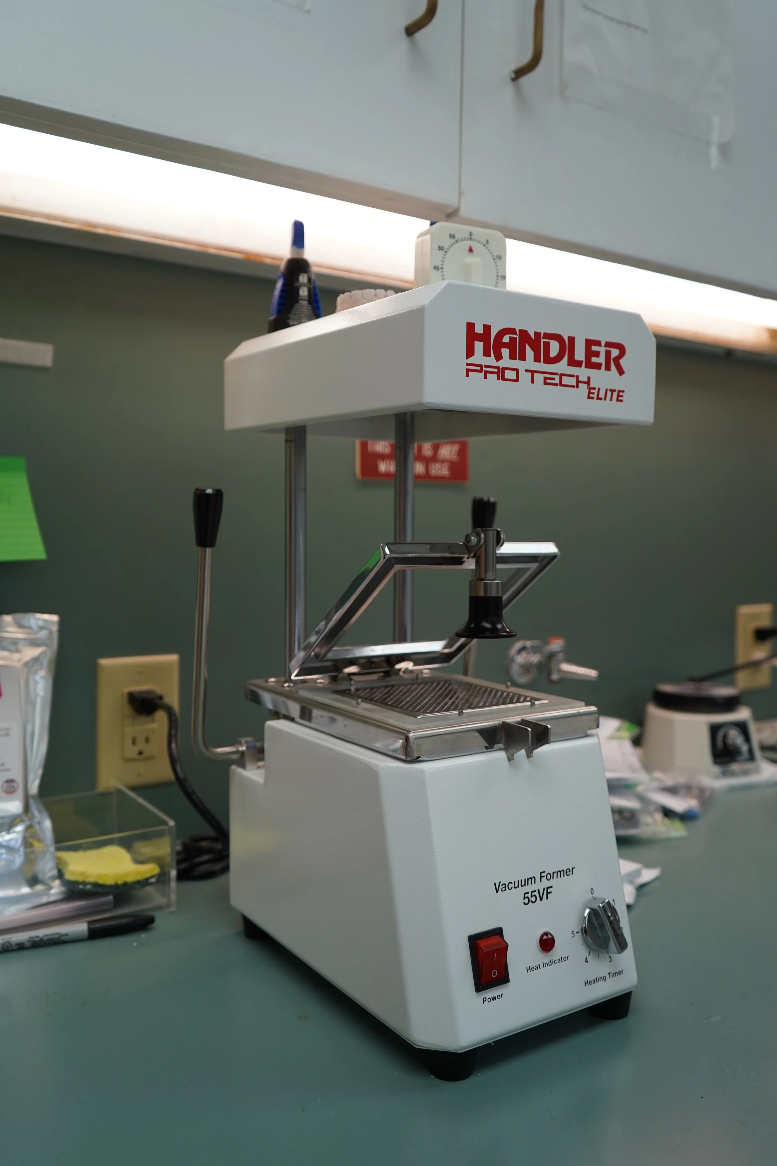 A laboratory vacuum forming machine labeled "Handler Pro Tech Elite" on a gray countertop, with various tools and papers around it.