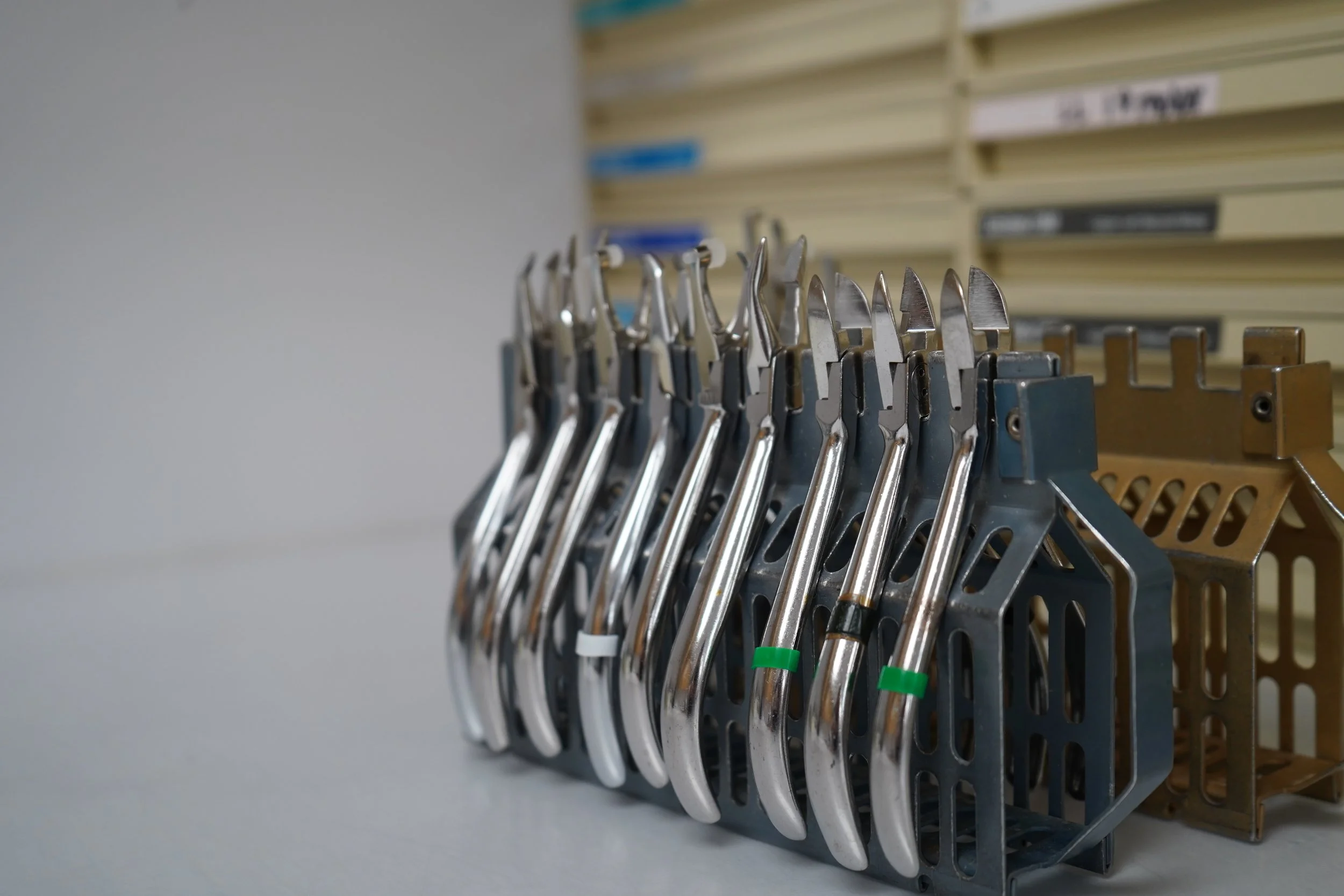 A row of surgical or dental tools with metal handles and various blade or hook ends, organized on a metal display rack in a medical or clinical setting.