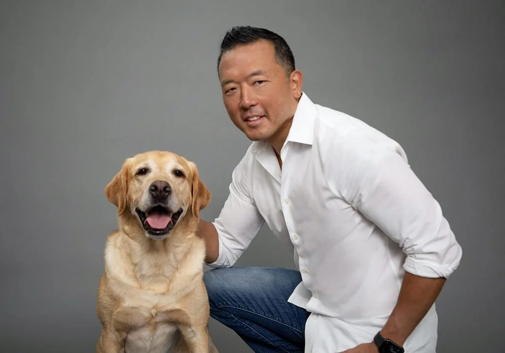 Michael Shikashio knealing next to a yellow lab