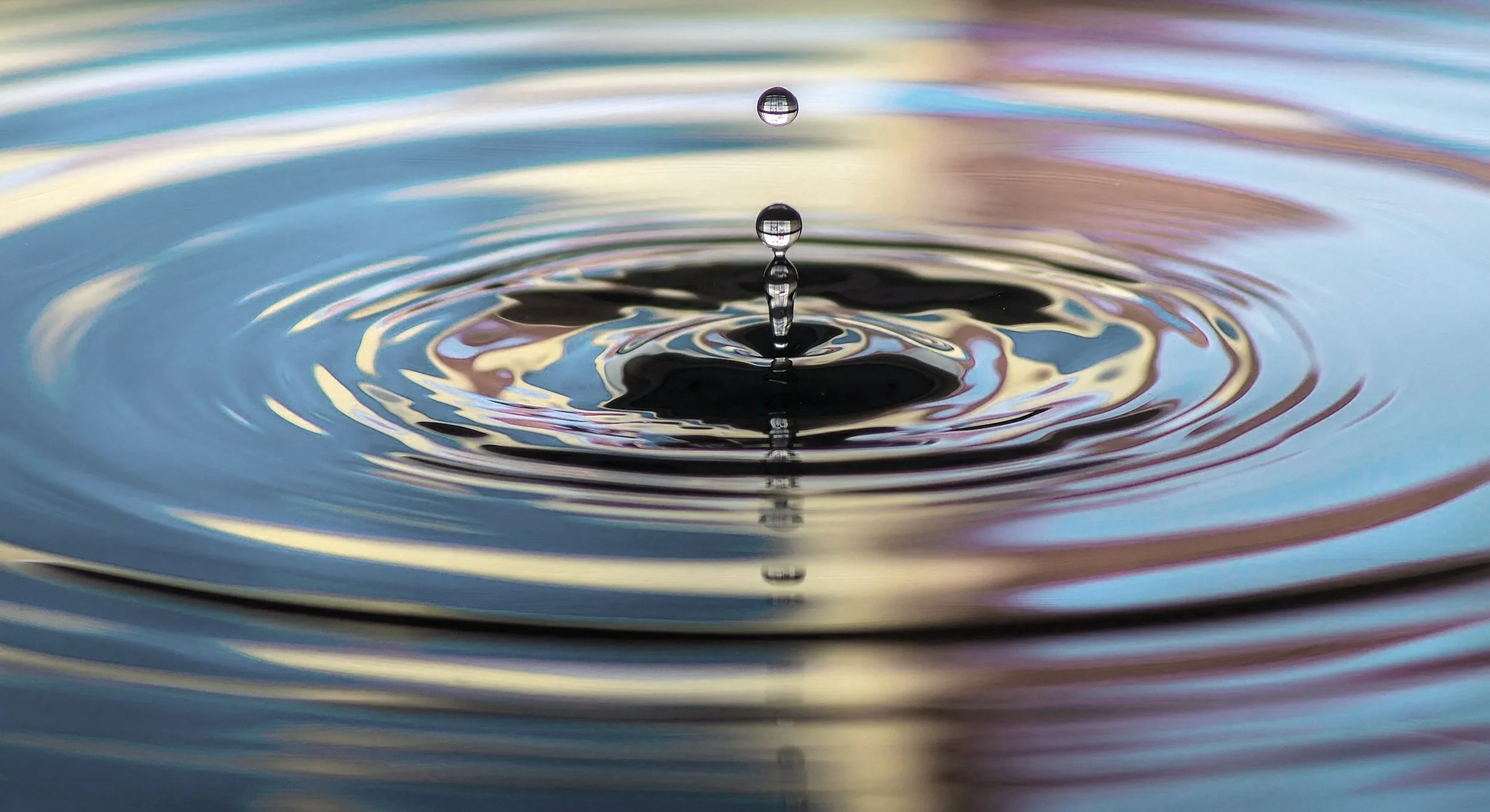Close-up of a water droplet falling into a calm body of water, creating ripples.