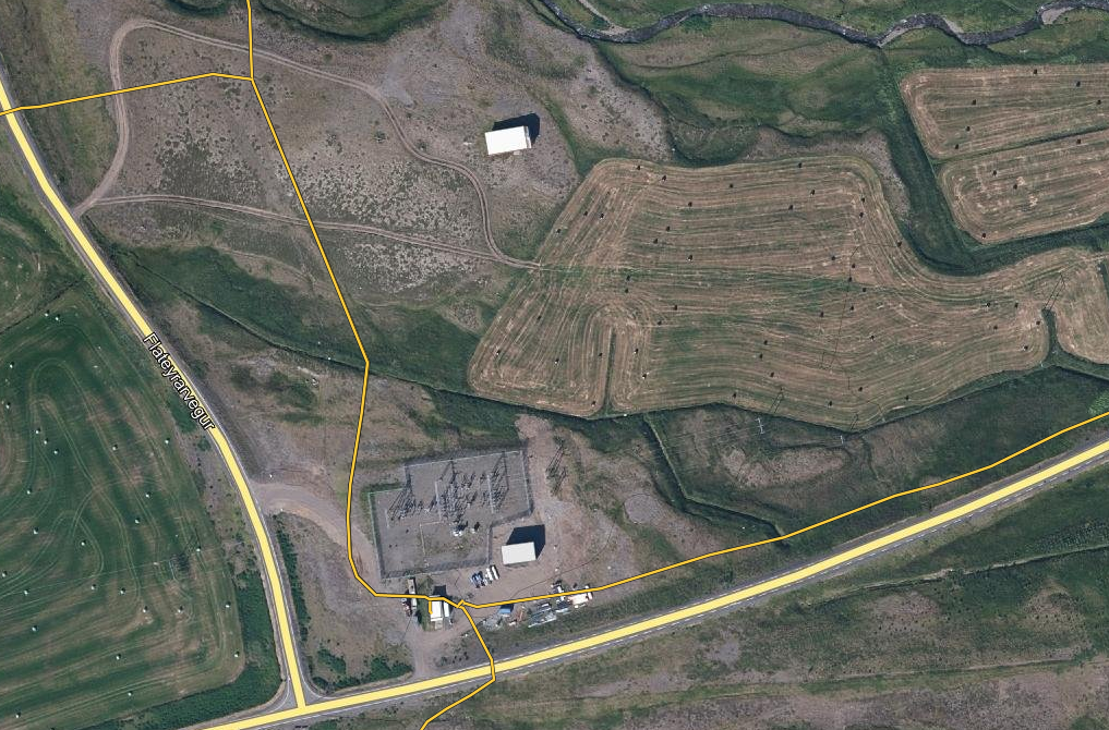 Aerial view of a rural landscape with fields, roads, and utility infrastructure, including a power substation surrounded by fencing.