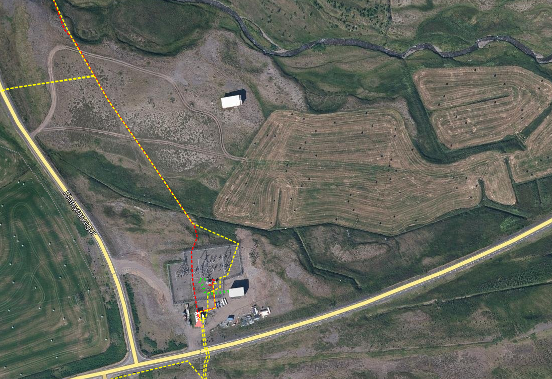 Aerial view of a rural landscape with fields, roads, a small building, and dashed lines indicating different paths or boundaries.