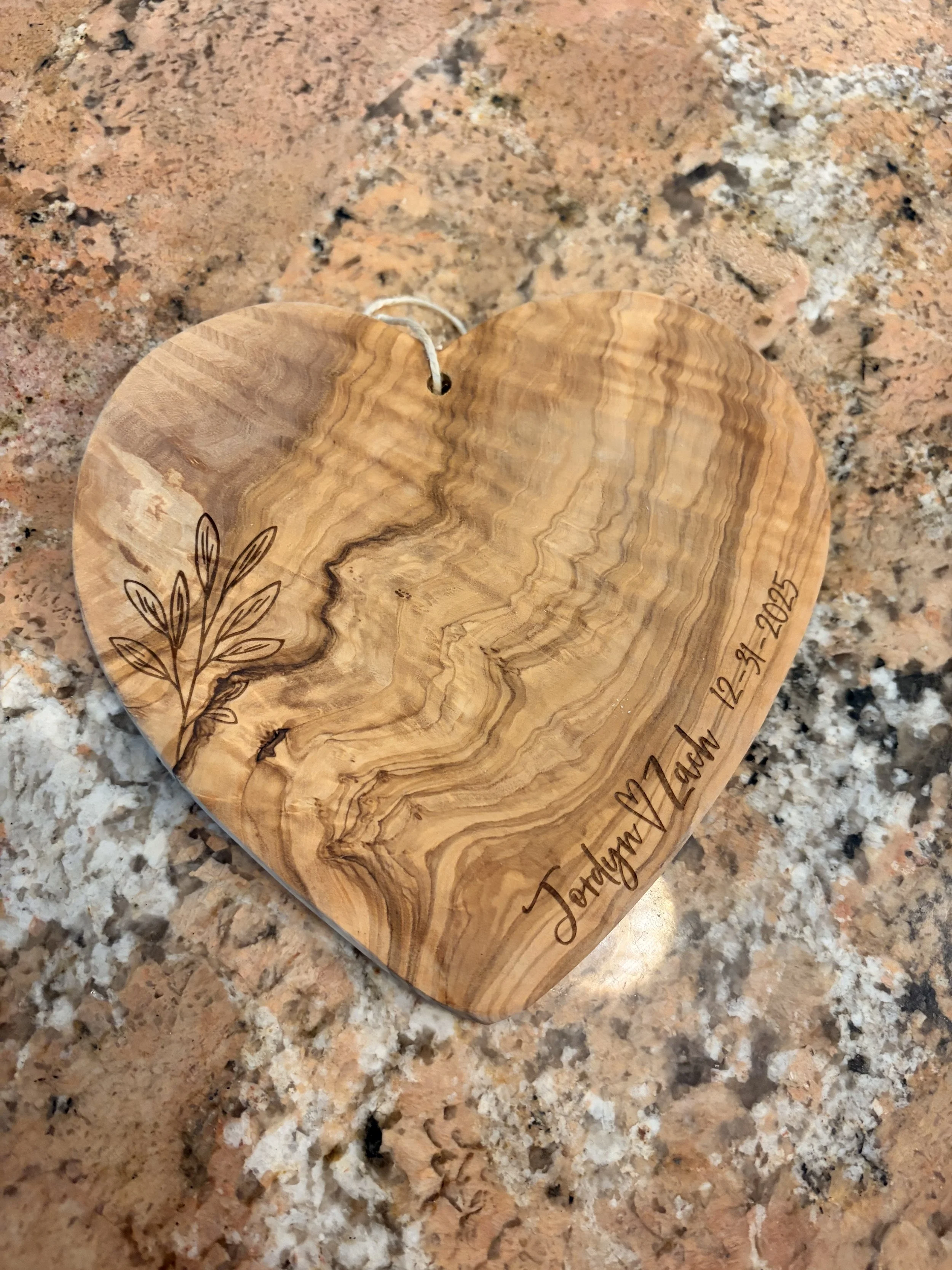 A wooden heart-shaped trivet with engraved text and branch to celebrate that special couple