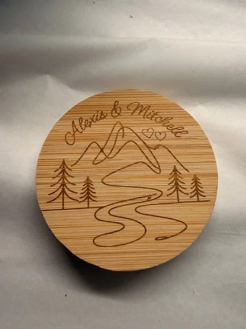 Wooden round bottle opener magnent with engraved mountains, trees, a river,