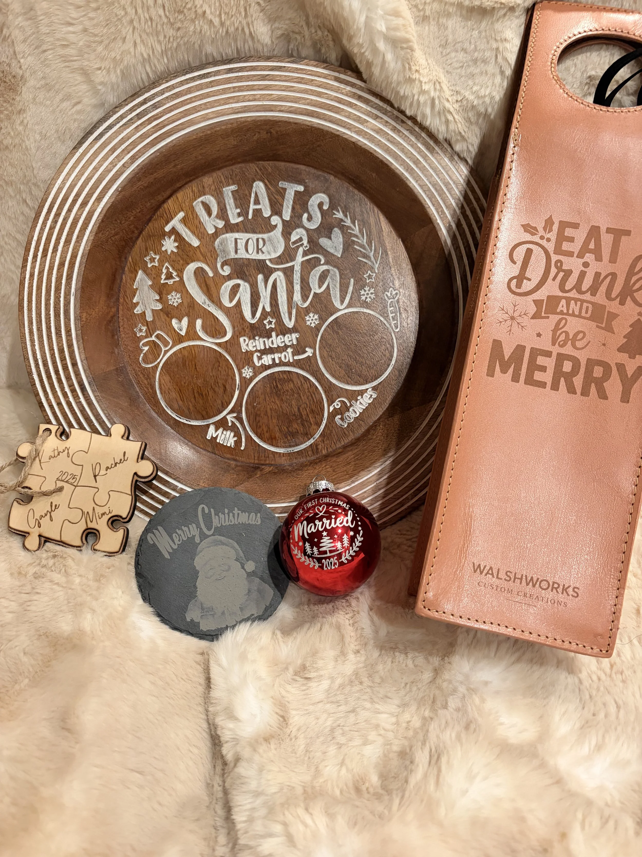 Holiday-themed decorative items on a soft beige surface, including a wooden tray with holiday design, a puzzle piece ornament , a slate coaster item, Wine bag and custom engraved glass ornament