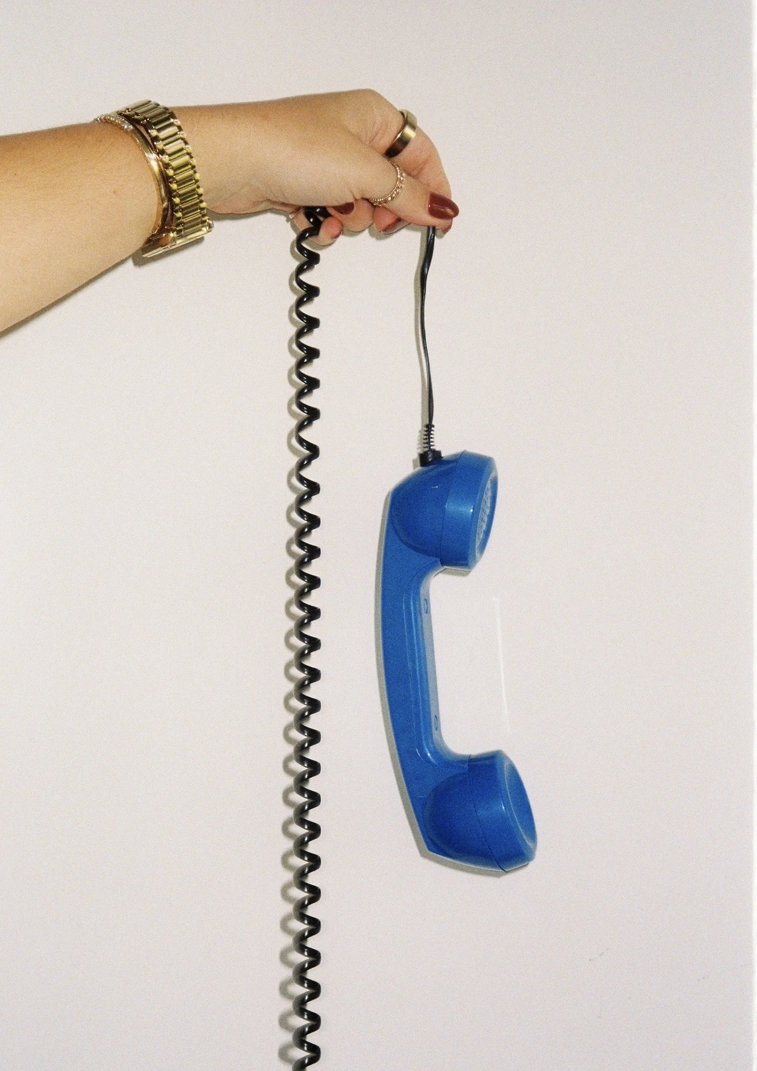 A person's hand holding a blue corded telephone handset by its cord against a plain white background.