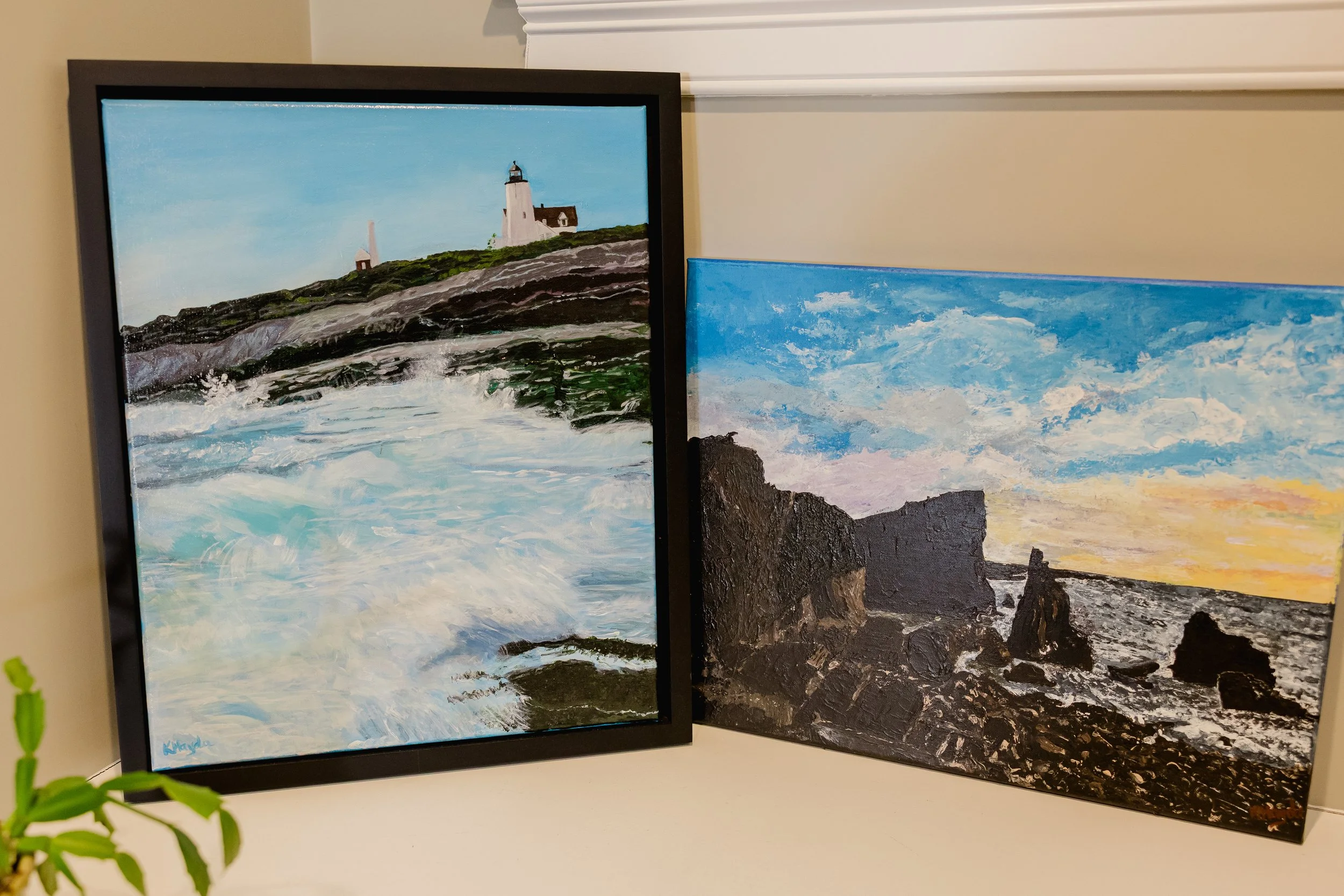 Two landscape paintings of the coast, one with a lighthouse and waves, the other with rocky cliffs and a sunset sky.