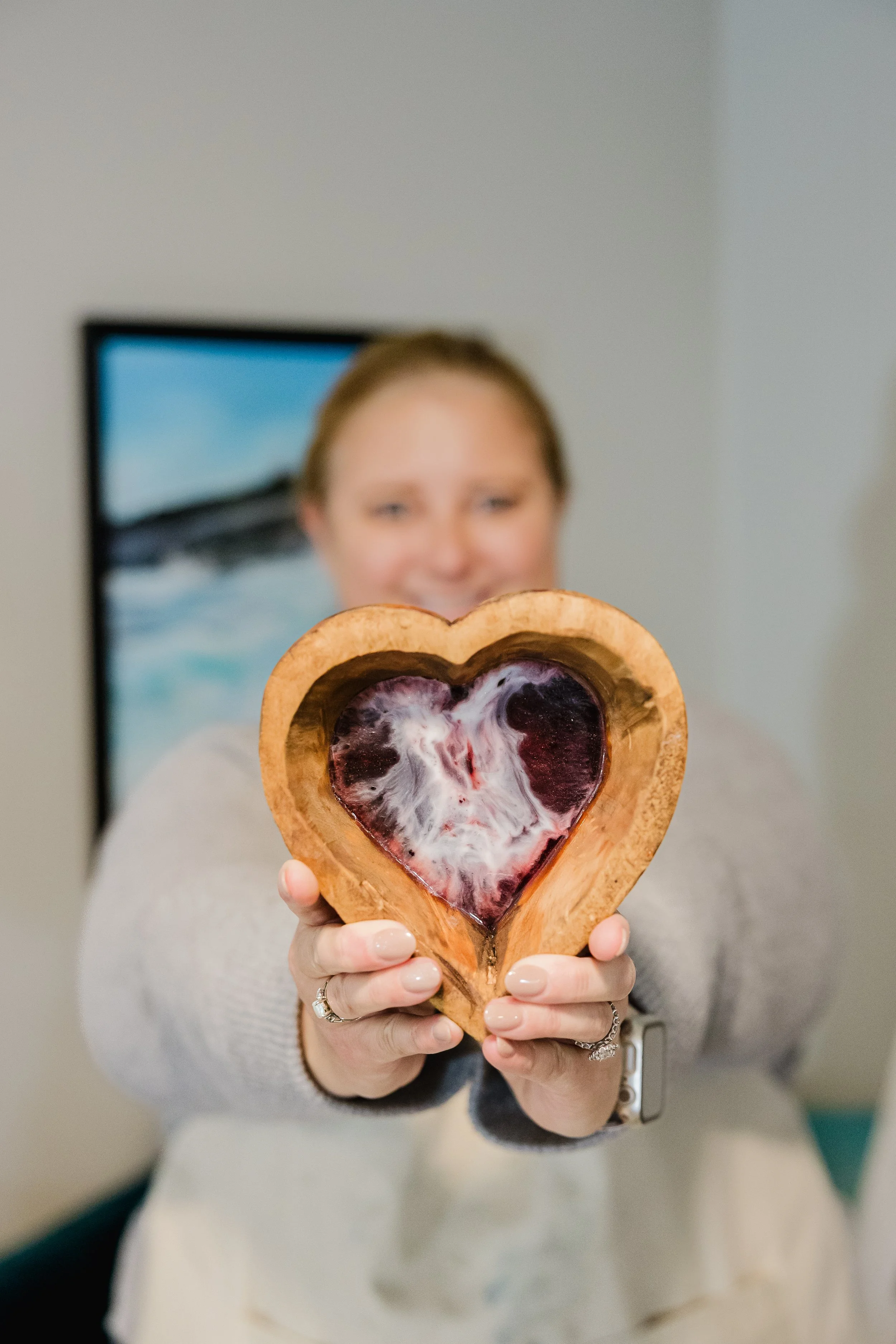 A woman holding a heart-shaped wooden dish with a purple heart-shaped jelly inside, smiling in the background.
