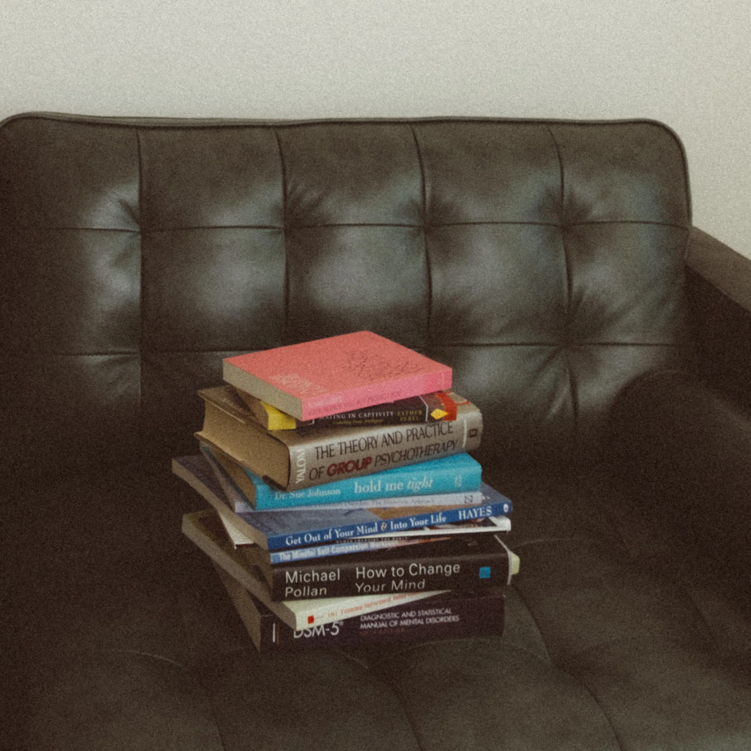 Stack of psychology and self-help books on a dark leather couch.