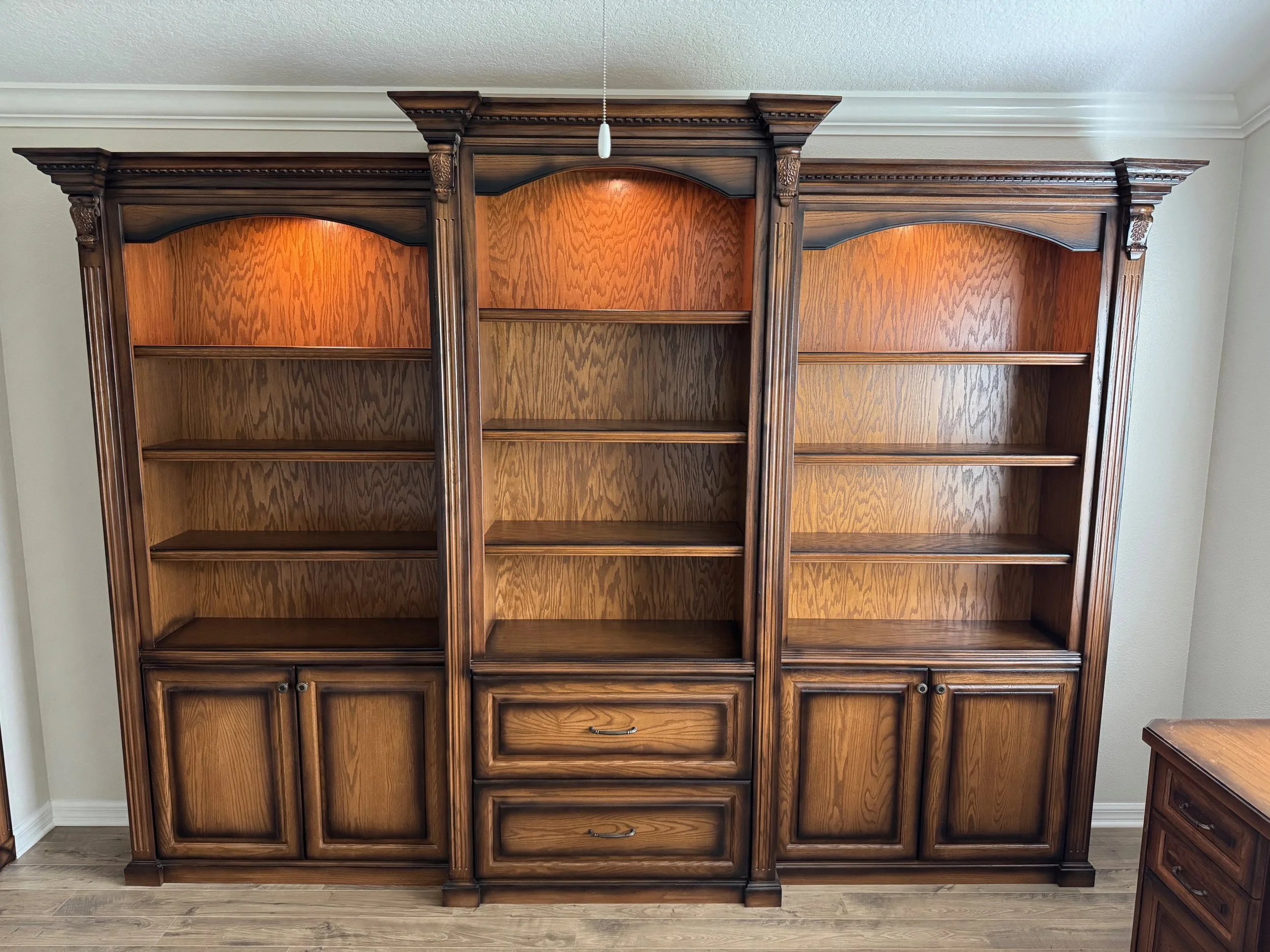 Large wooden bookshelf with three sections, each with shelves and lower cabinet doors, against a white wall in a room with wood flooring.