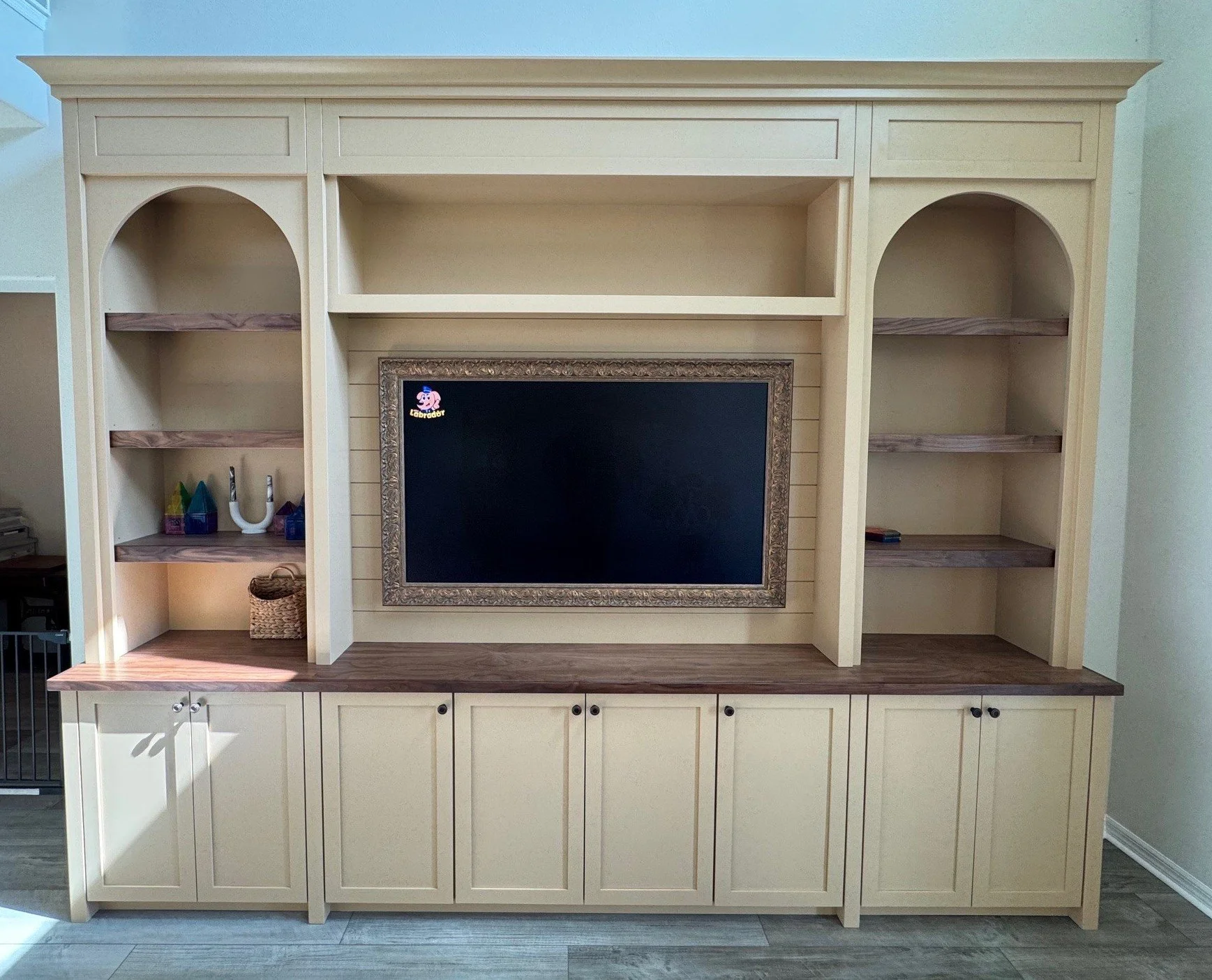 9. A classic touch for the modern home. This custom wall unit features elegant arched shelving, a framed TV display, and rich wood tones countertops that contrast beautifully with the warm cream cabinetry.