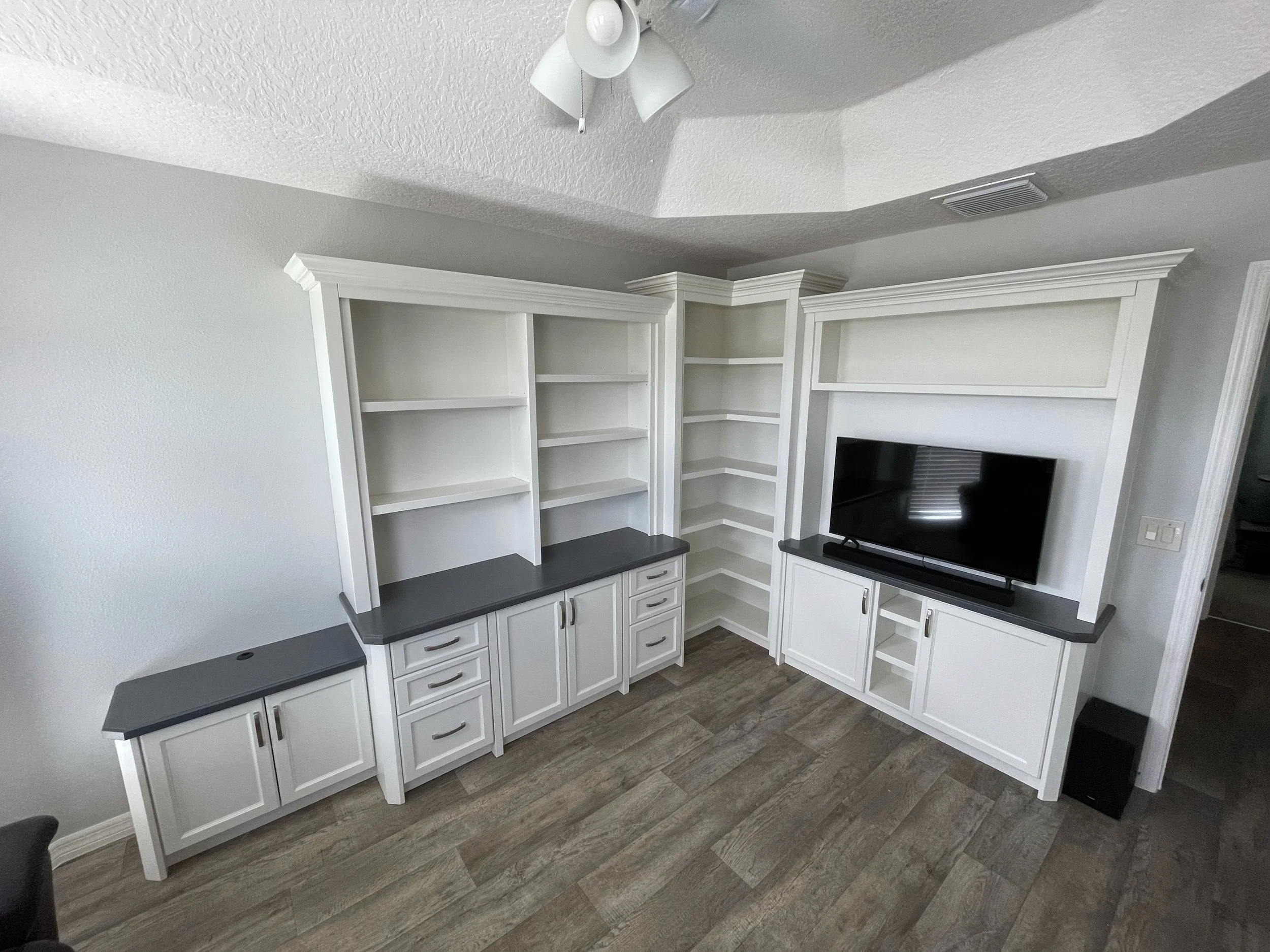 16. Maximize every inch of your room with a custom corner entertainment suite. This expansive design features bright white cabinetry, contrasting charcoal countertops, and a specialized wraparound shelving unit to turn an awkward corner into a seamle