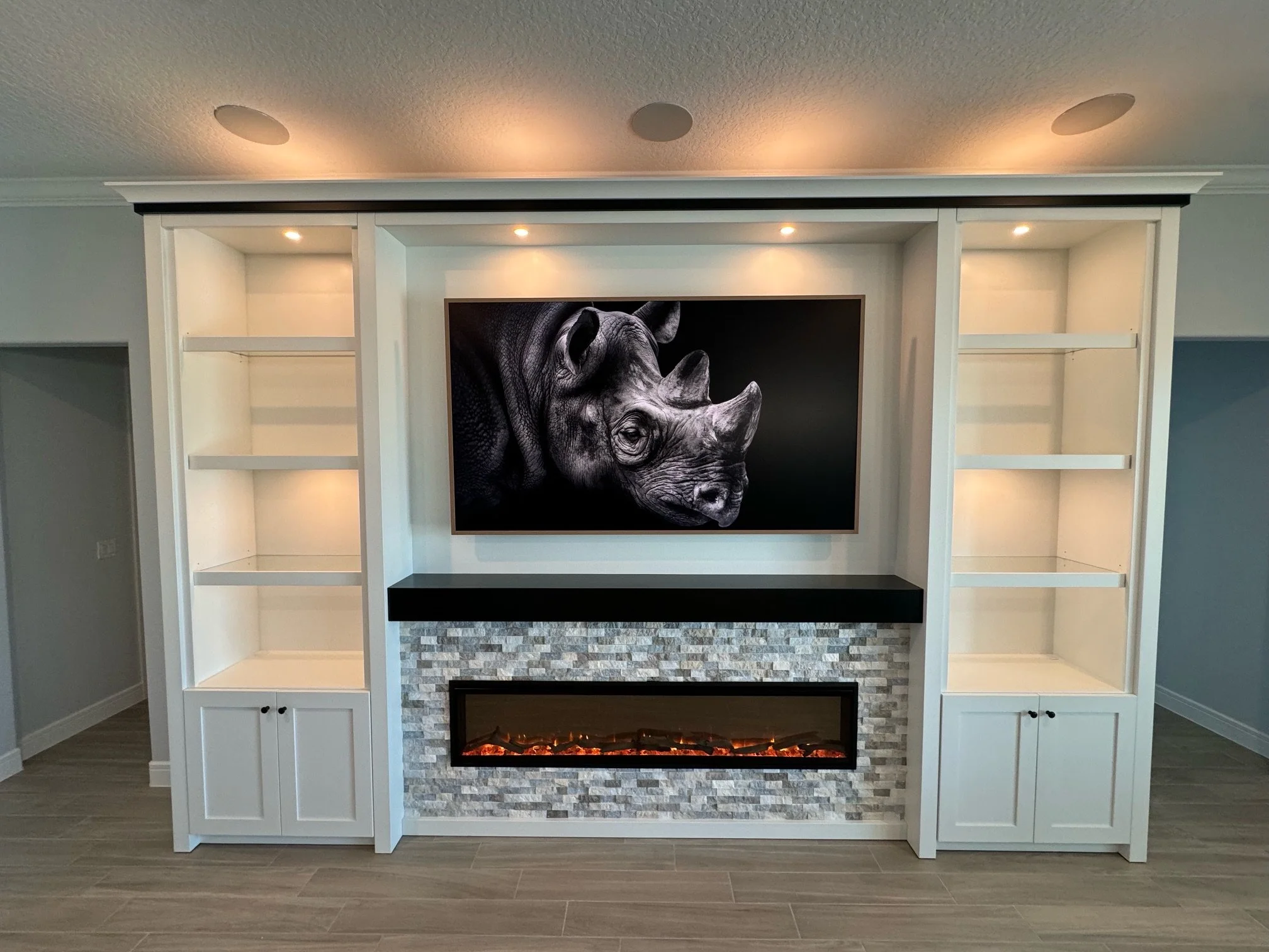 3. Clean lines meet contemporary warmth. This custom wall unit features a sleek black mantel, a textured stone fireplace, and integrated lighting that perfectly frames the art and shelving for a bold living room statement.