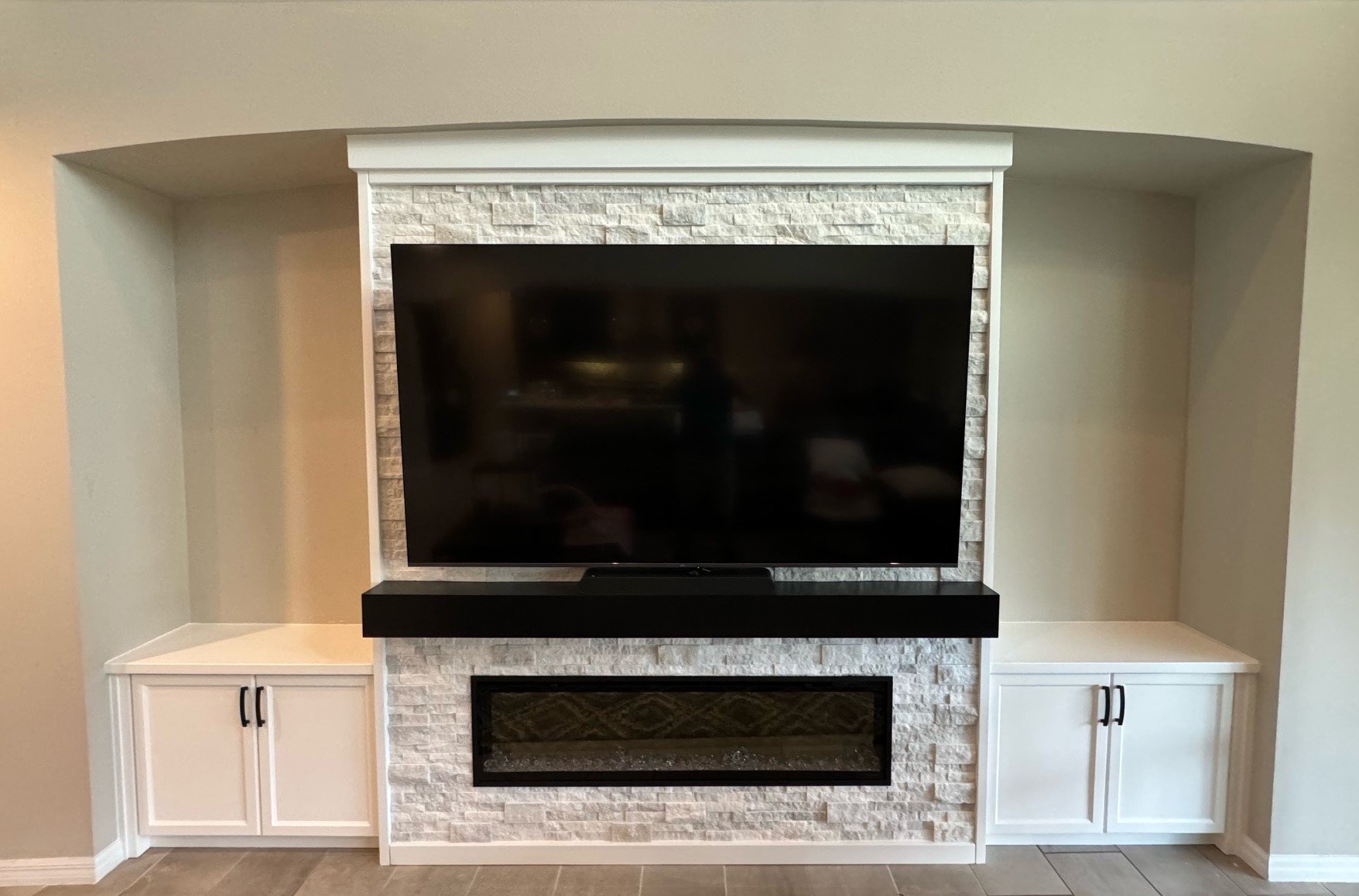 15. Clean and contemporary. This custom unit features bright white cabinetry, a textured stone surround, and a bold black mantle that perfectly anchors the electric fireplace and media center.