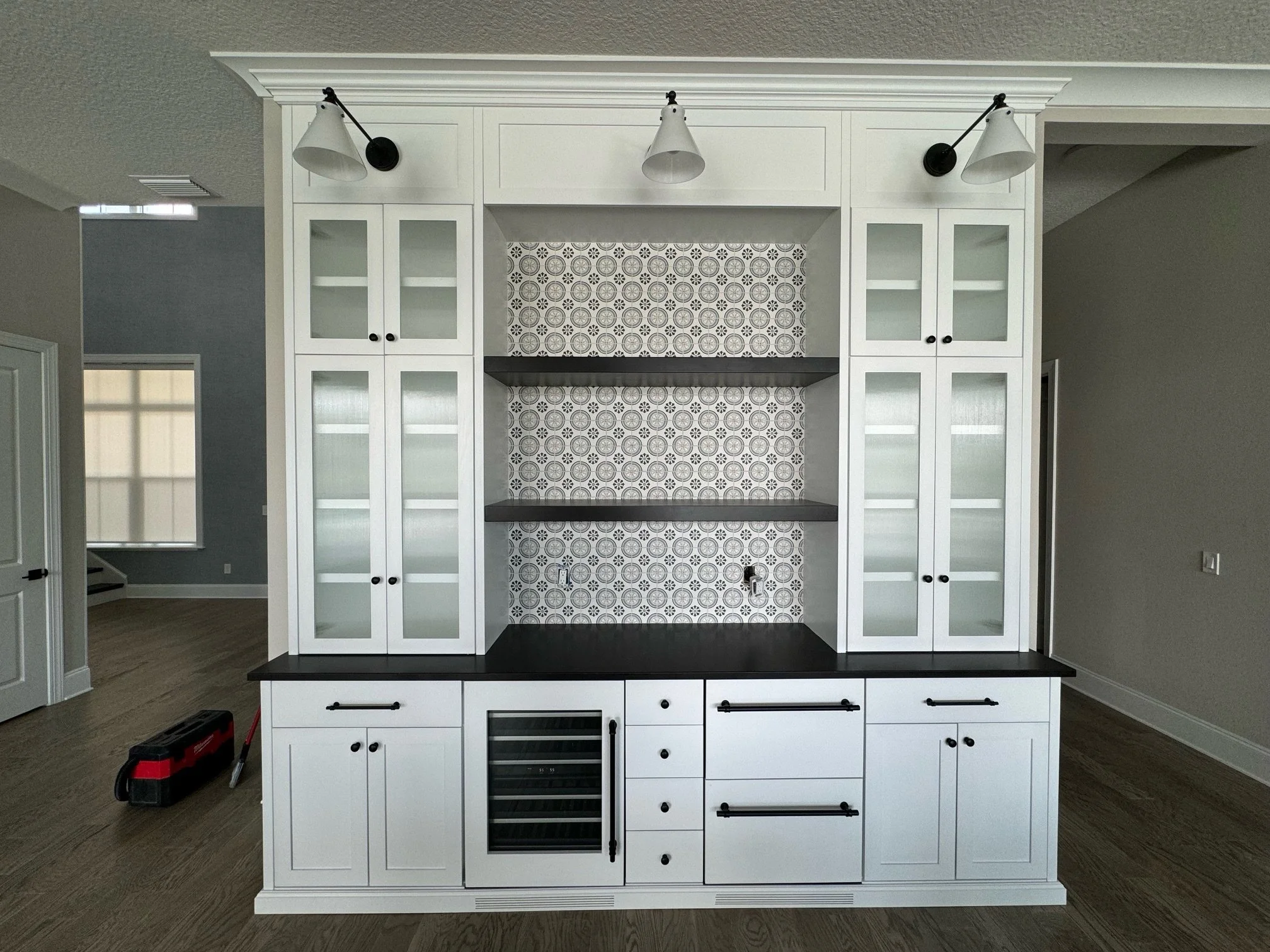 3. Modern entertaining made easy. This custom white dry bar features a stunning patterned tile backsplash, contrasting black countertops, and integrated wine refrigeration. The glass cabinetry and industrial-style gooseneck lighting add the perfect t