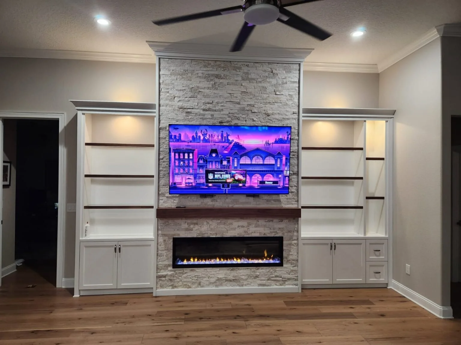 1. This custom wall unit features a stunning floor-to-ceiling stone fireplace, sleek integrated shelving with warm accent lighting, and a seamless media setup designed for the ultimate living room experience
