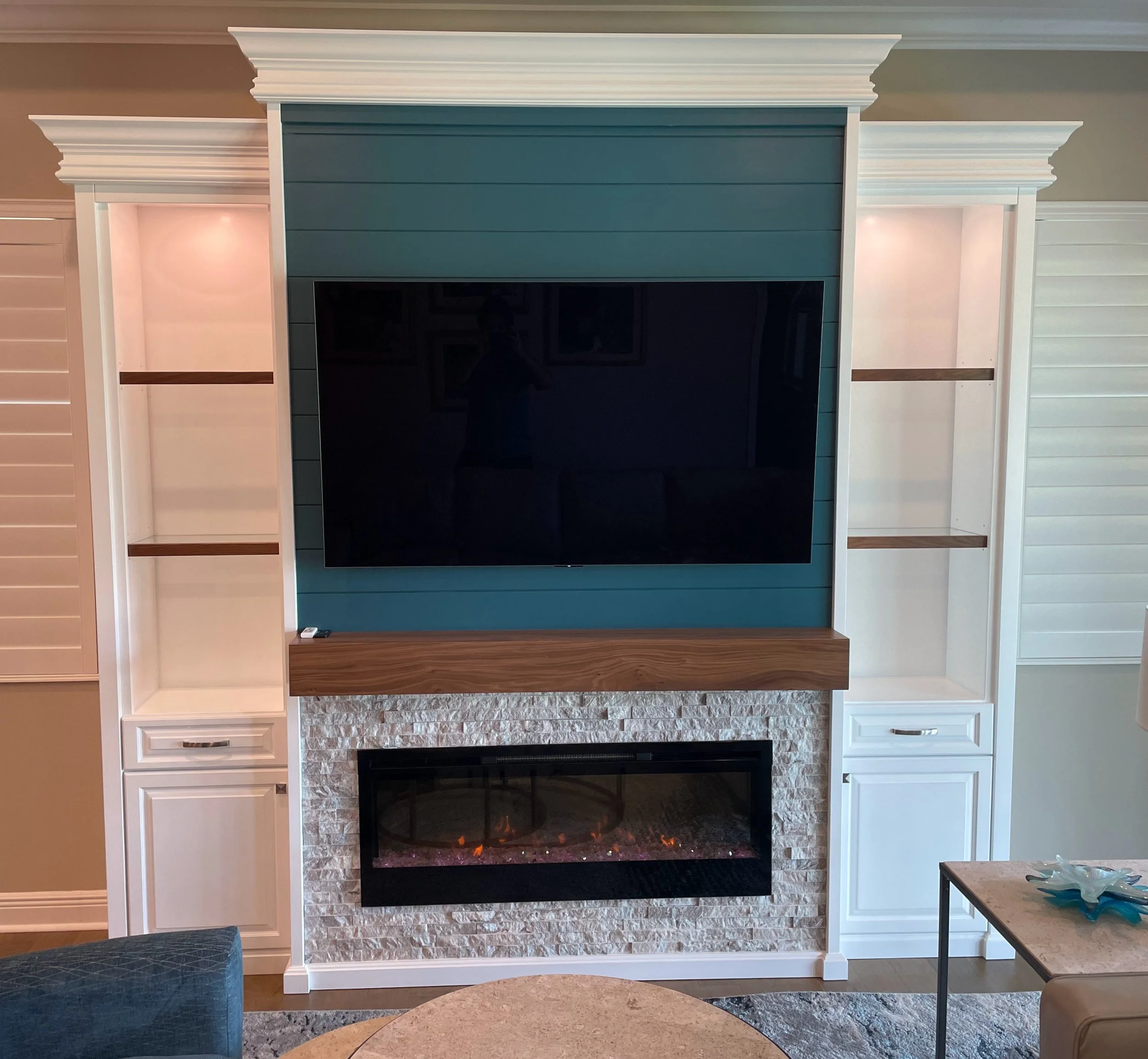 54. Make a splash with a sophisticated teal shiplap focal point. This custom wall unit blends modern texture with organic warmth, featuring a natural stone fireplace, a rich walnut mantle, and elegant white cabinetry with glass-inset shelving.
