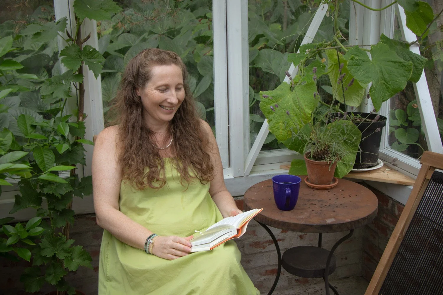 Kvinne som leser bok i drivhuset omgitt av grønne planter.