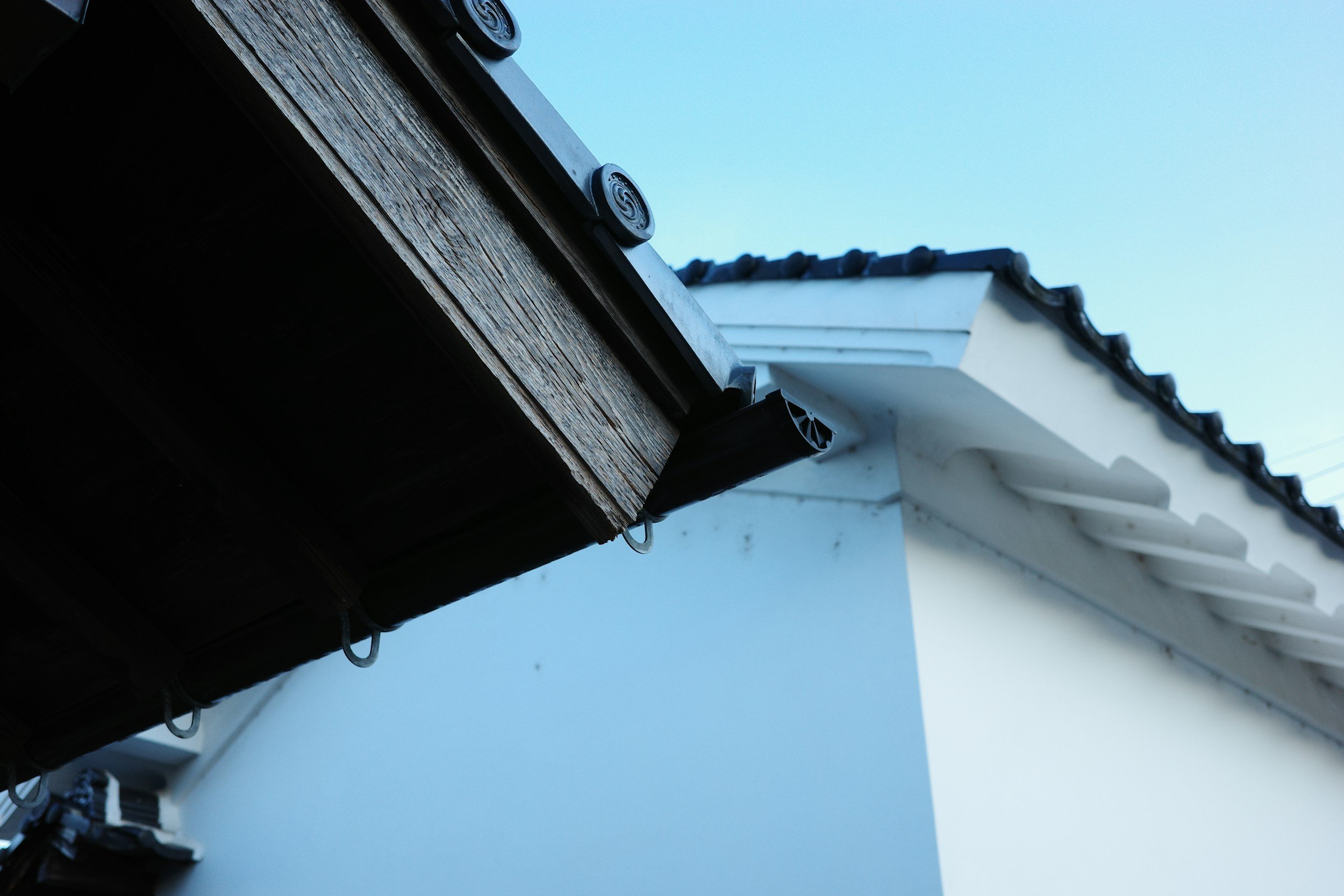 Close-up van een dakgoot en dakrand van een wit huis met blauwe hemel op de achtergrond.