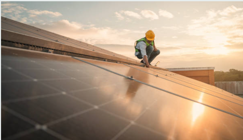 Werknemer op het dak van een gebouw, installeert zonnepanelen bij zonsondergang.