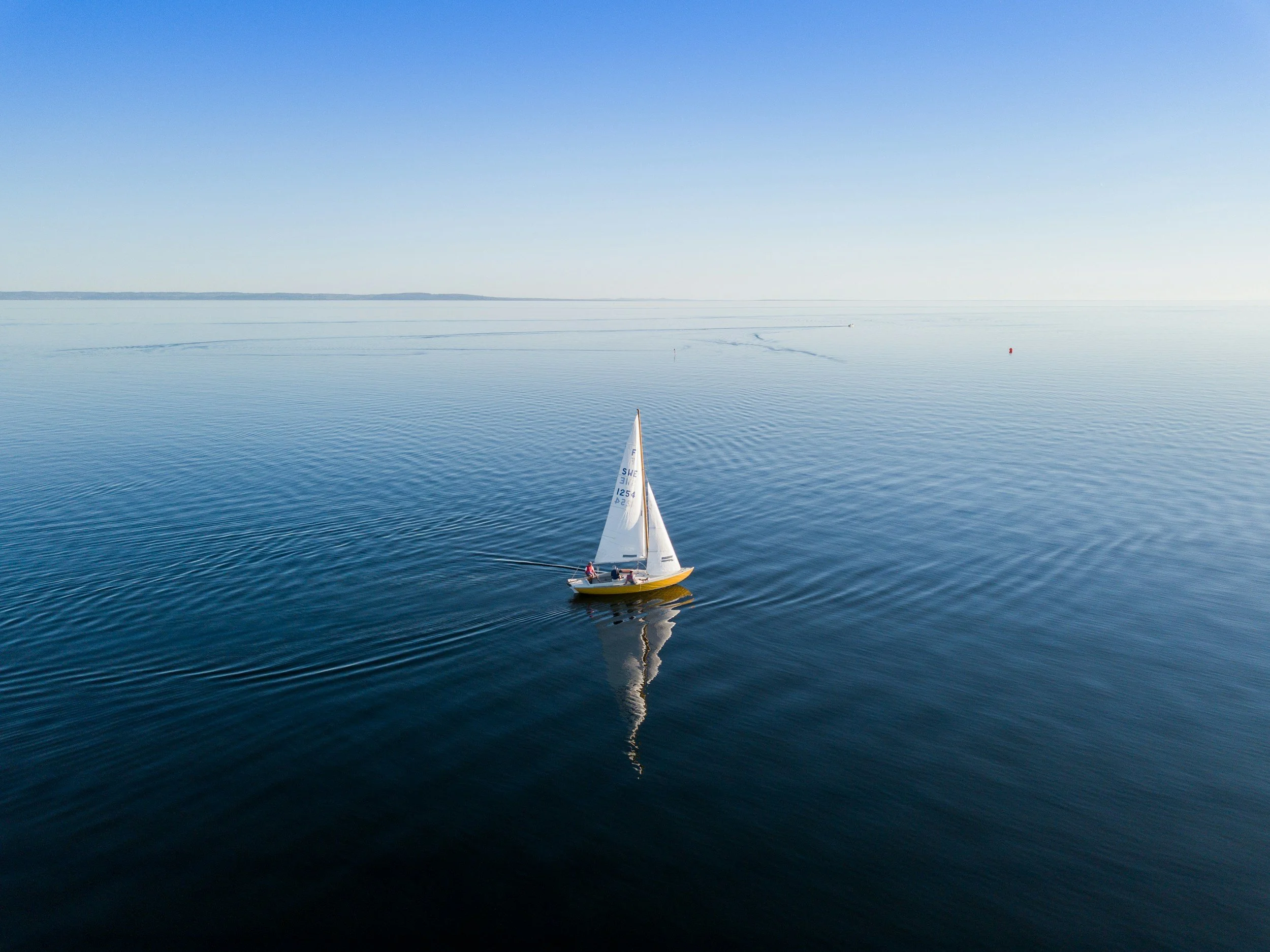 Ein Segelboot auf ruhigem Wasser mit klarem blauen Himmel im Hintergrund.