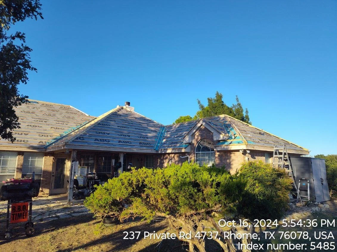 A house under renovation with a partially installed roof, a ladder on the side, and a bush in the front yard, located at 237 Private Rd 4737 in Rhome, Texas, on October 16, 2024.