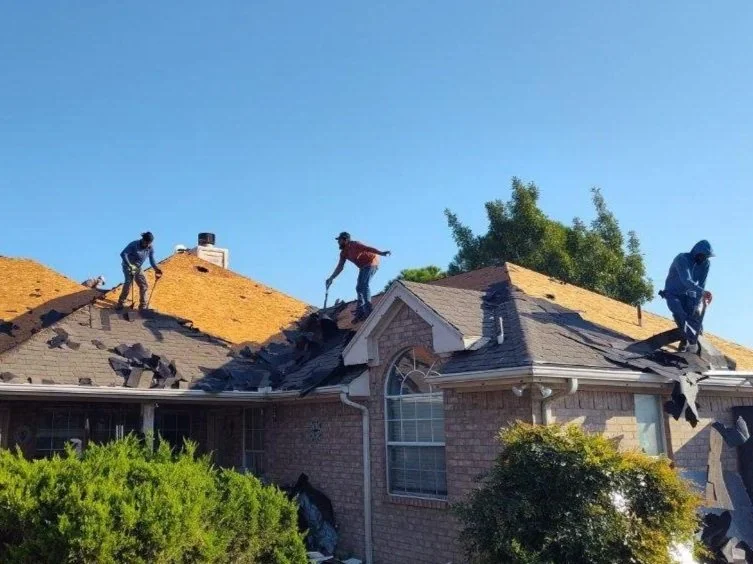 Three workers on a house roof removing old shingles on a sunny day.