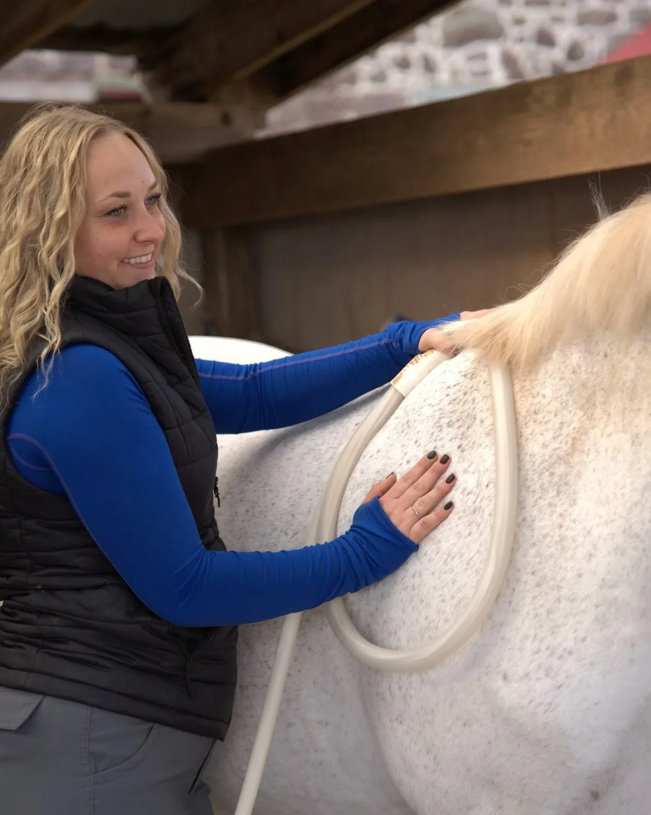 A woman in a blue shirt and black vest is smiling while holding a PEMF Magnawave attachment