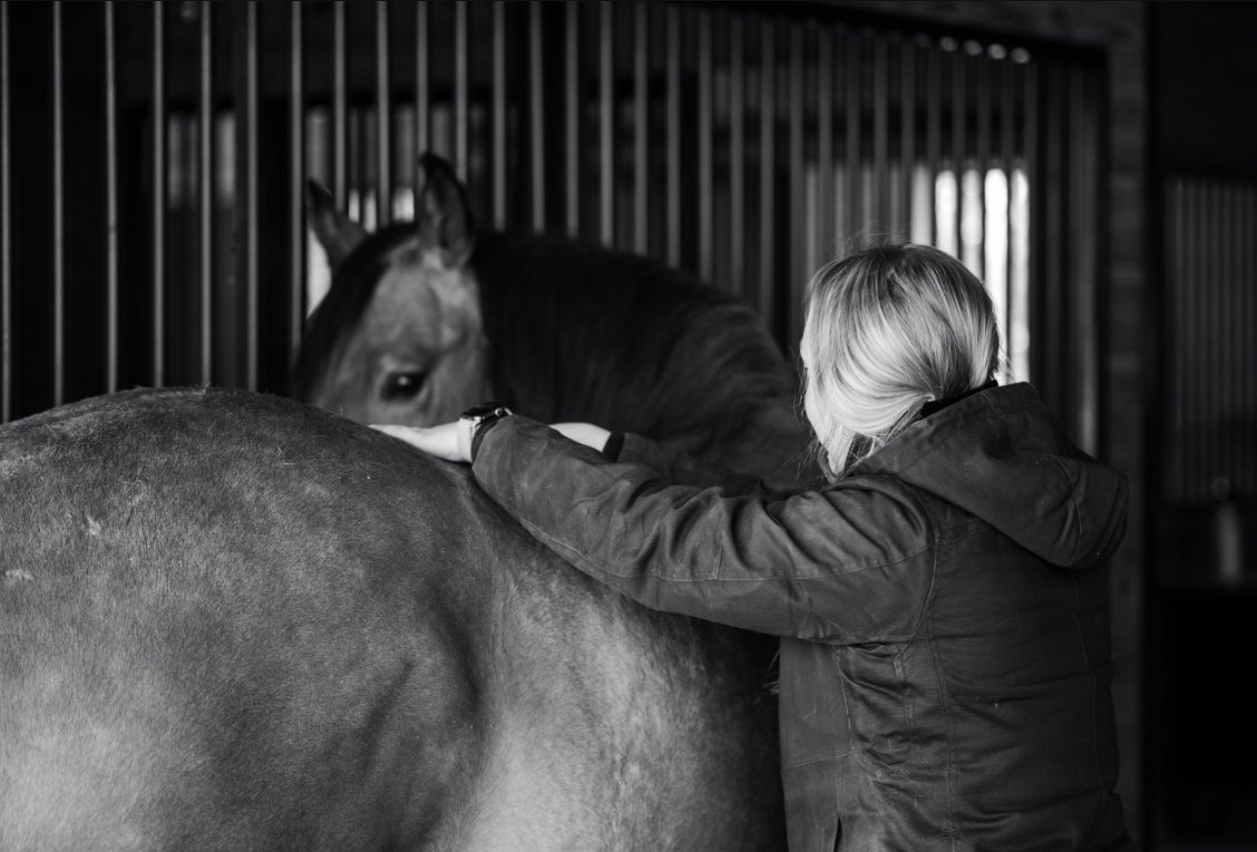 A person interacting with a horse inside a stable, black and white photo.