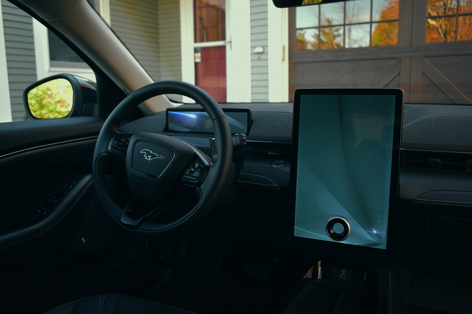 Interior of a modern car with a digital dashboard, steering wheel with a logo, and a large smartphone on the passenger side, with a house and trees visible through the windows.